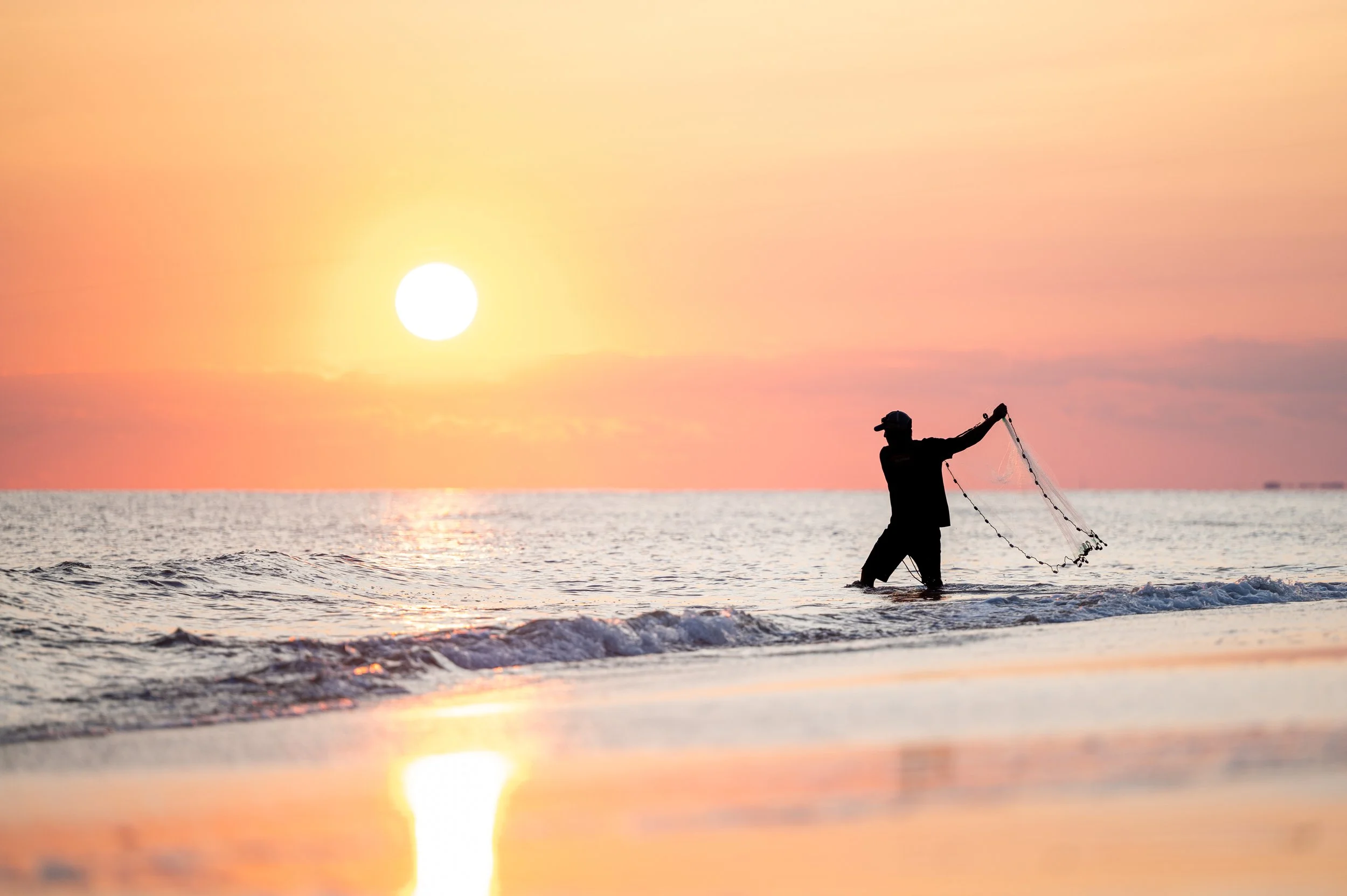 Fisherman casting a net along the shoreline at sunset on Caswell Beach, North Carolina.