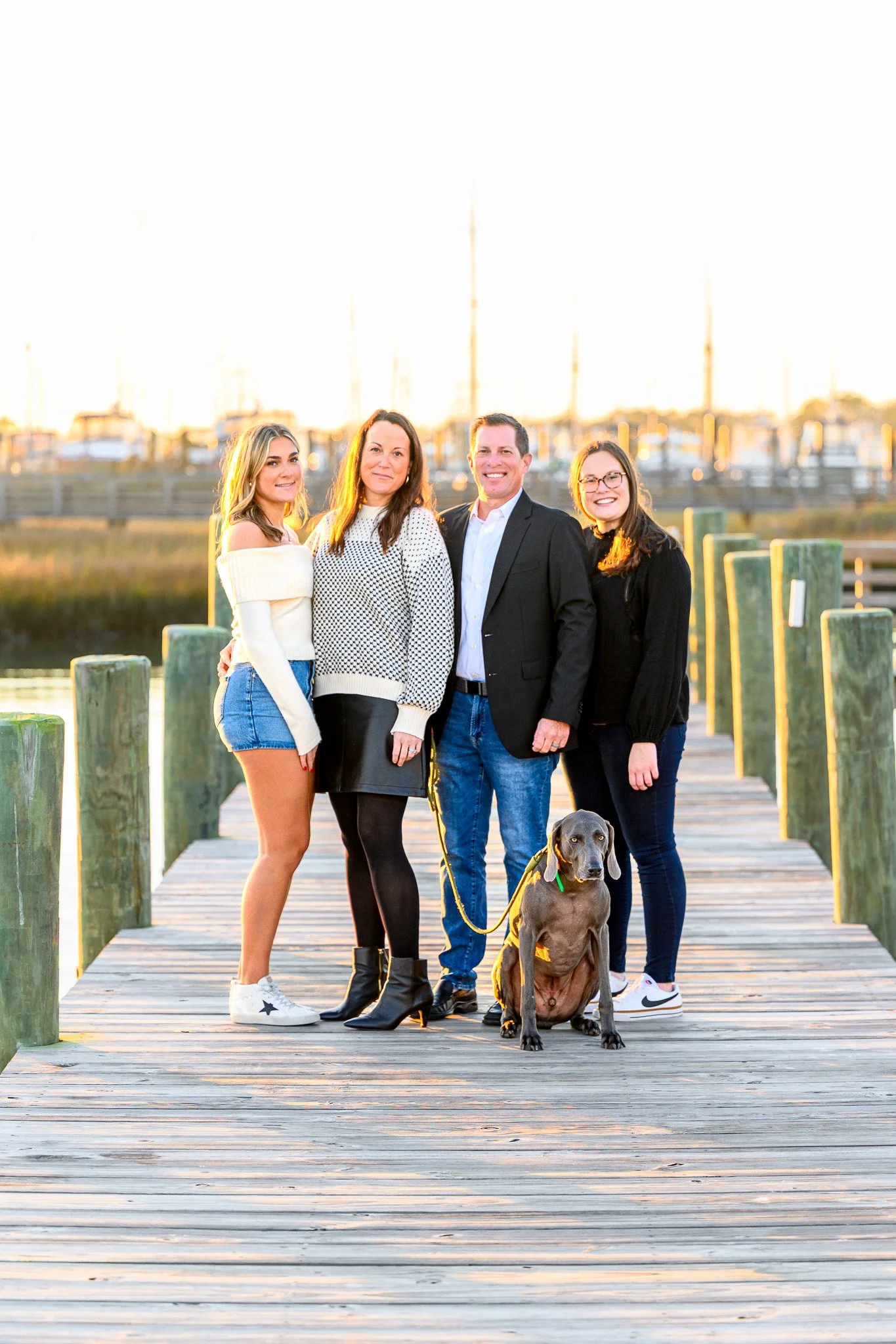 Family portrait on a marina dock in Southport with boats and the waterfront glowing in the evening light.
