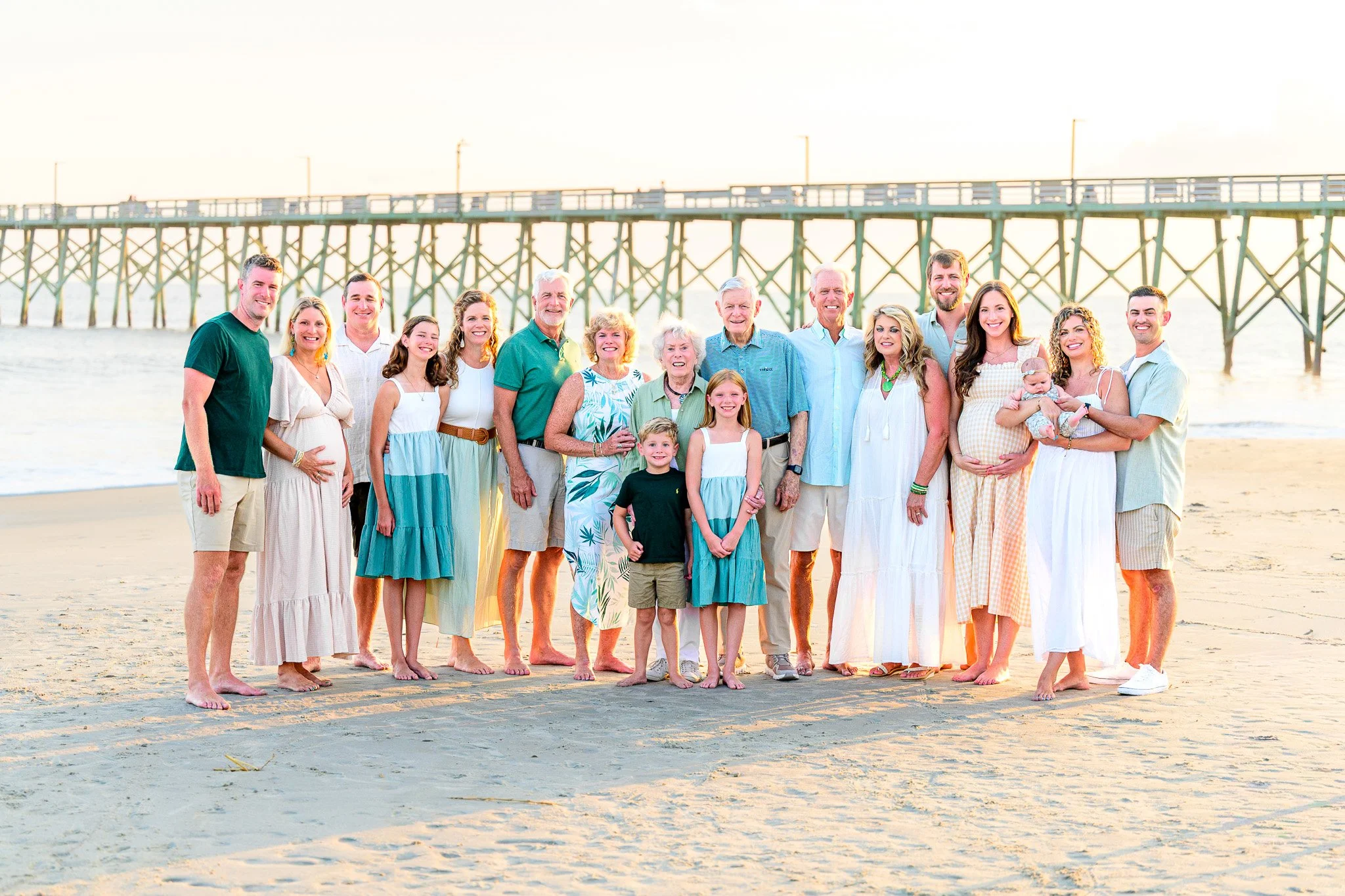 Extended family beach photography session at the Oak Island Pier featuring a multi-generation family with the sun glistening through the Oak Island Pier in the background at sunset