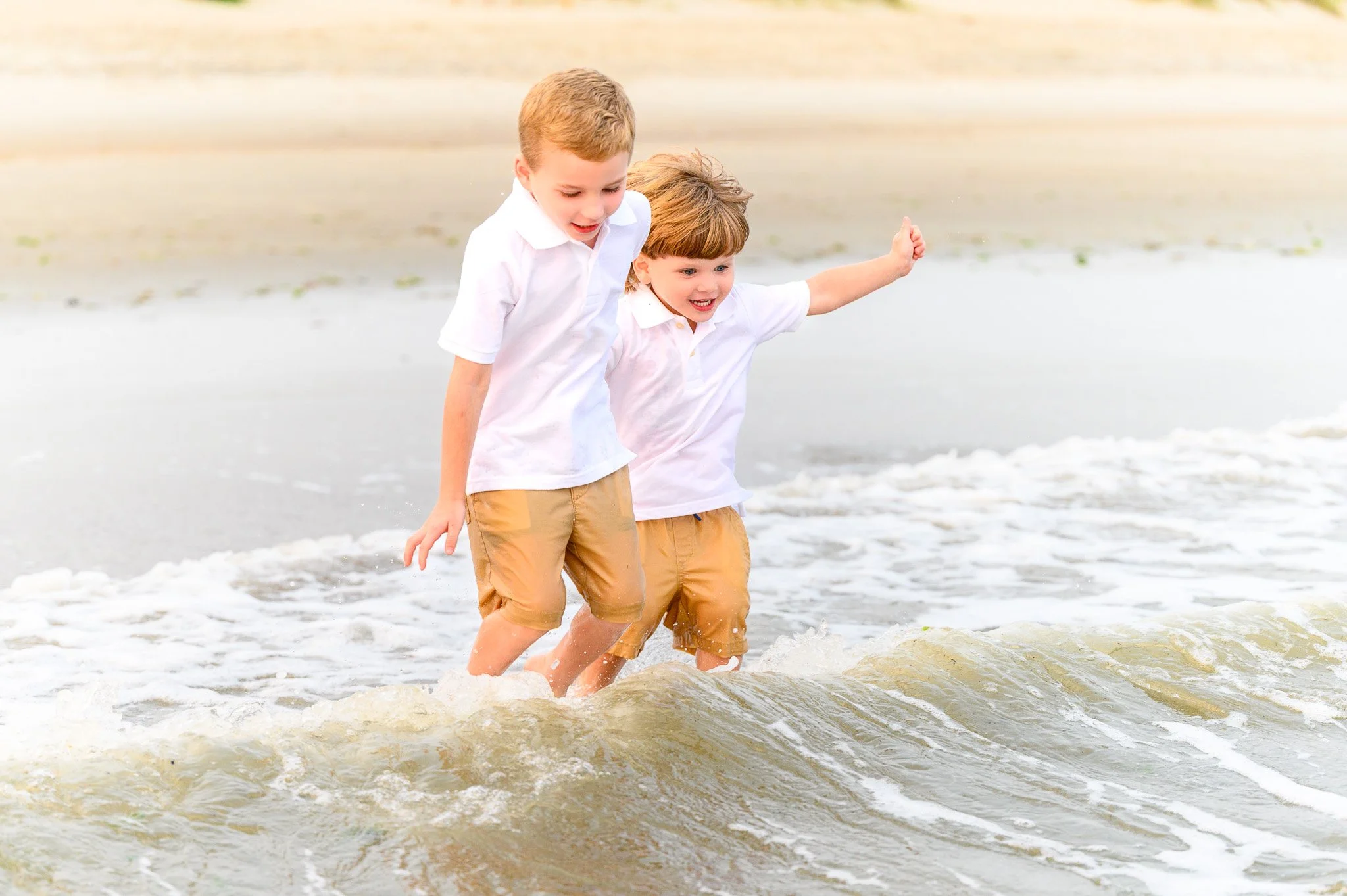 Two young boys playing in the gentle surf at Caswell Beach on Oak Island, North Carolina, a family-friendly beach with calm shoreline waters.