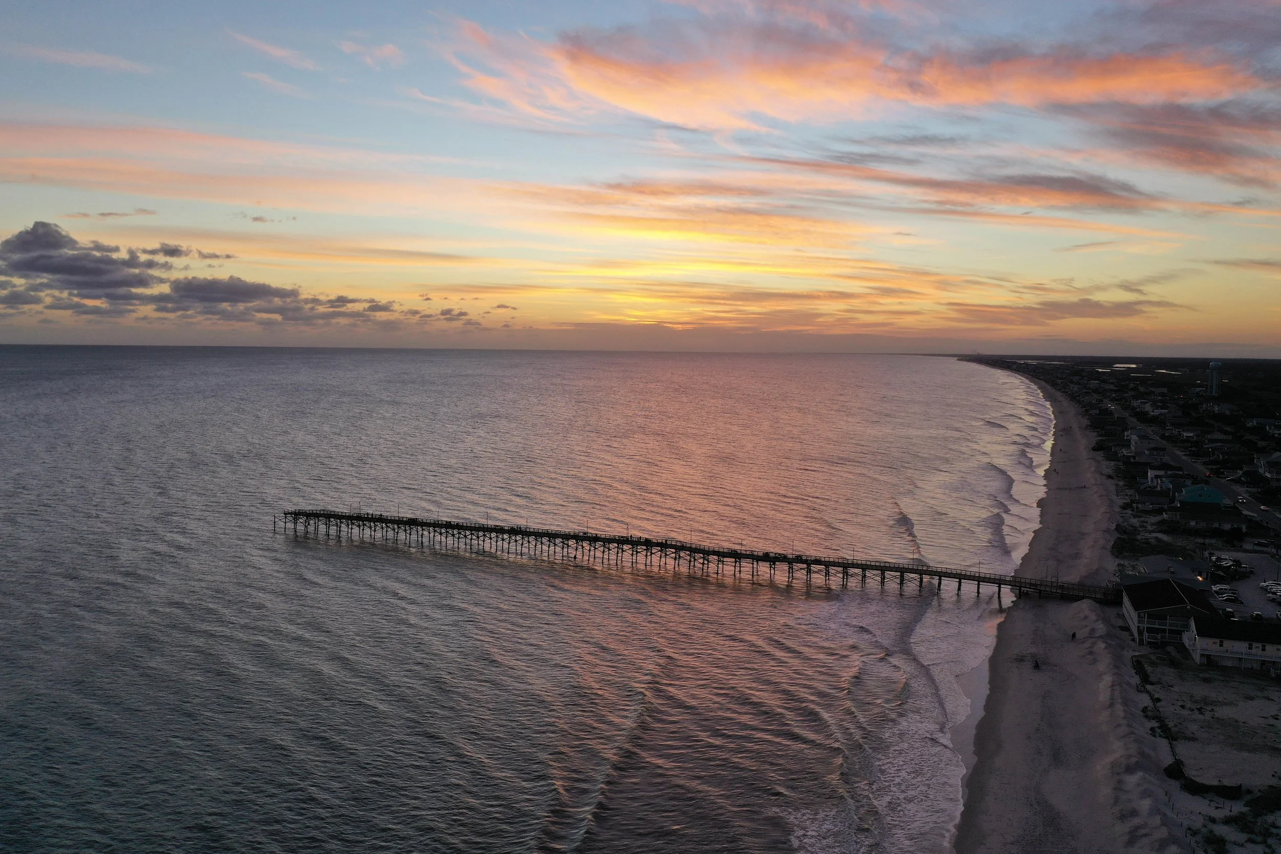 Aerial view of Ocean Crest Pier extending into the Atlantic Ocean at sunset on Oak Island, North Carolina.