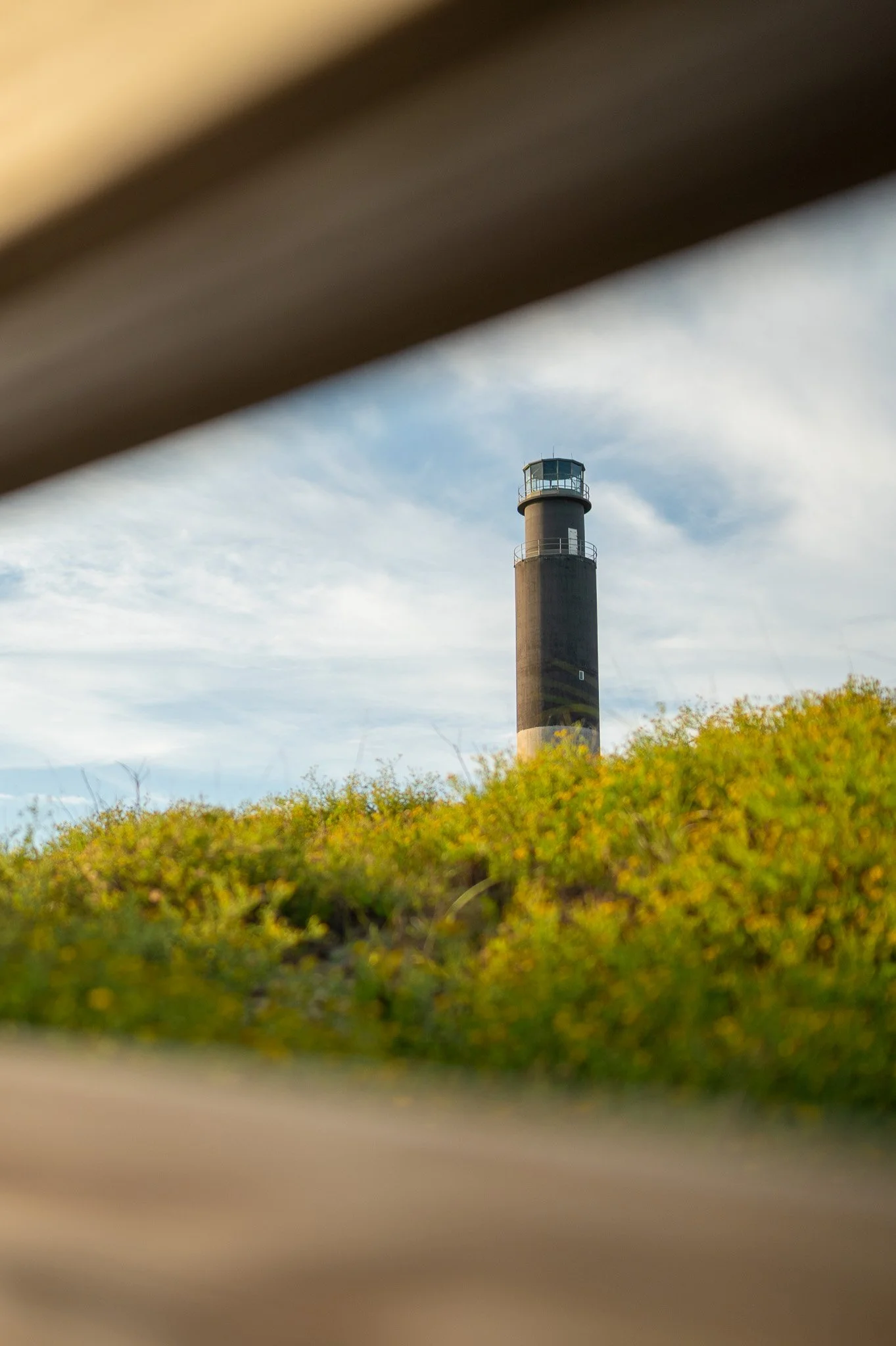 Oak Island Lighthouse viewed through a beach access boardwalk overlooking the dunes at Caswell Beach on Oak Island, North Carolina.