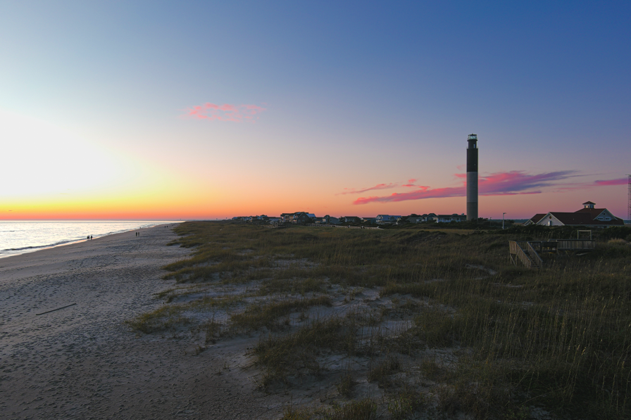 Sunset over Caswell Beach with the Oak Island Lighthouse rising above the dunes along the North Carolina coast.