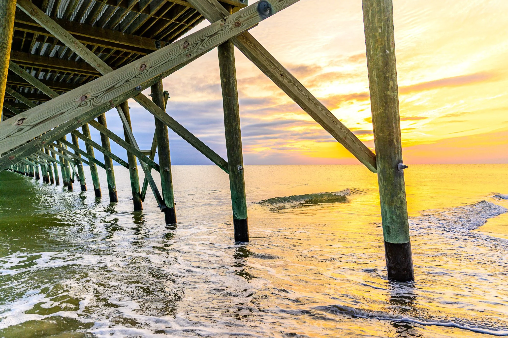 Sunrise view from beneath Oak Island Pier overlooking the Atlantic Ocean near oceanfront restaurants and dining on Oak Island, North Carolina.