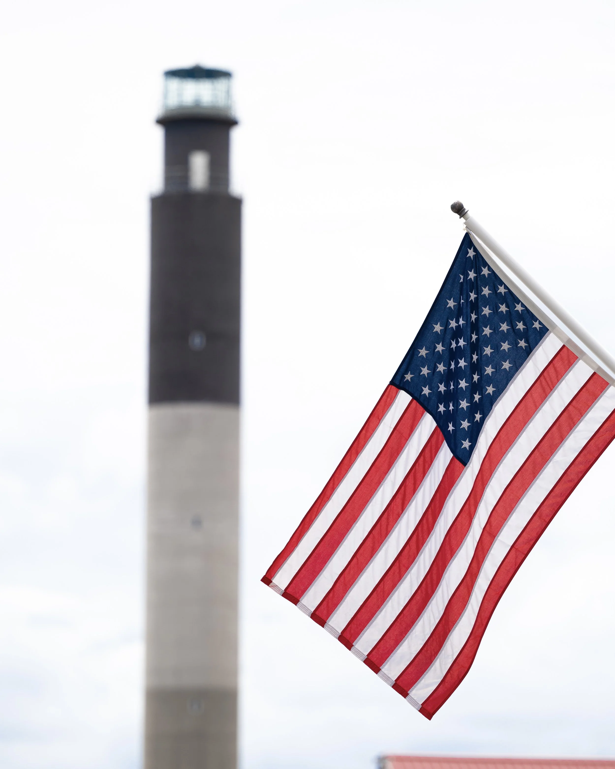 American flag waving with the Oak Island Lighthouse in the background at Caswell Beach on Oak Island, North Carolina.