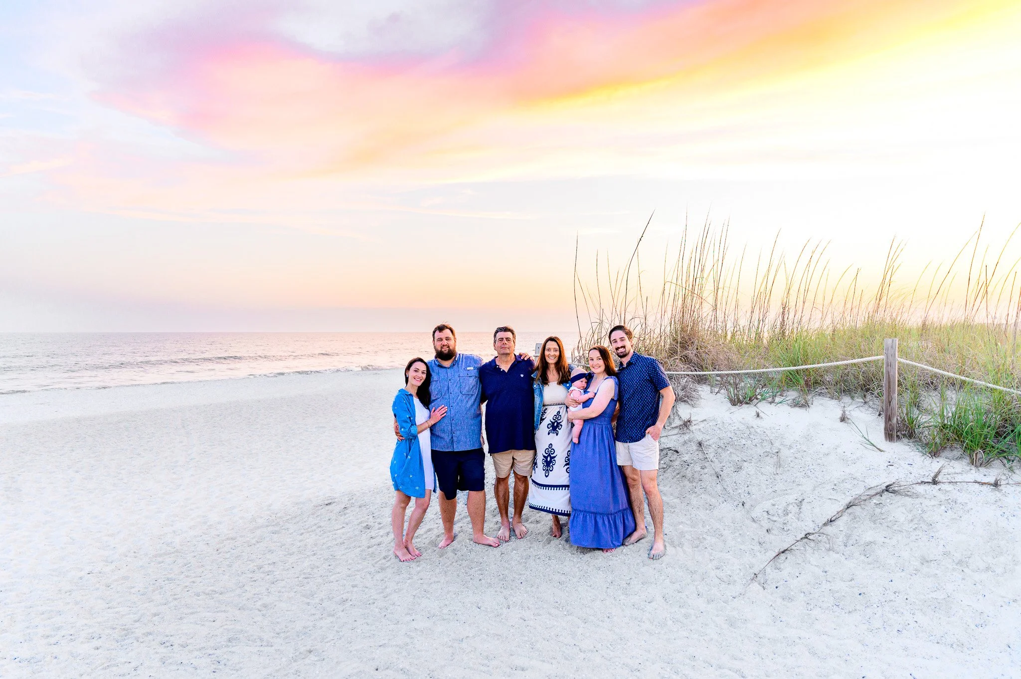 Family gathered on the beach at sunset with sea oats and pastel skies on Oak Island, North Carolina.