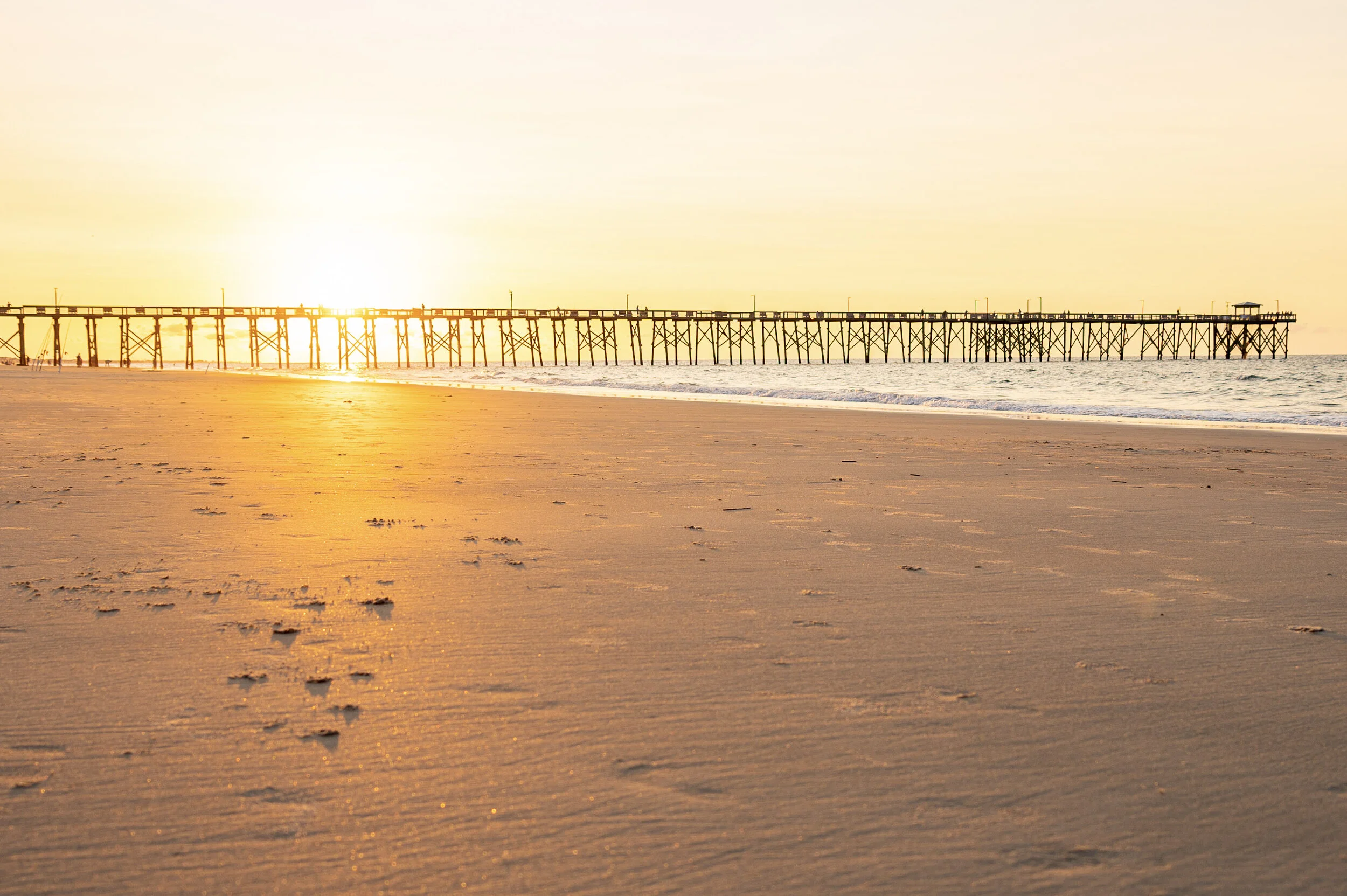 Oak Island Pier stretching into the Atlantic Ocean during sunrise on Oak Island, North Carolina.