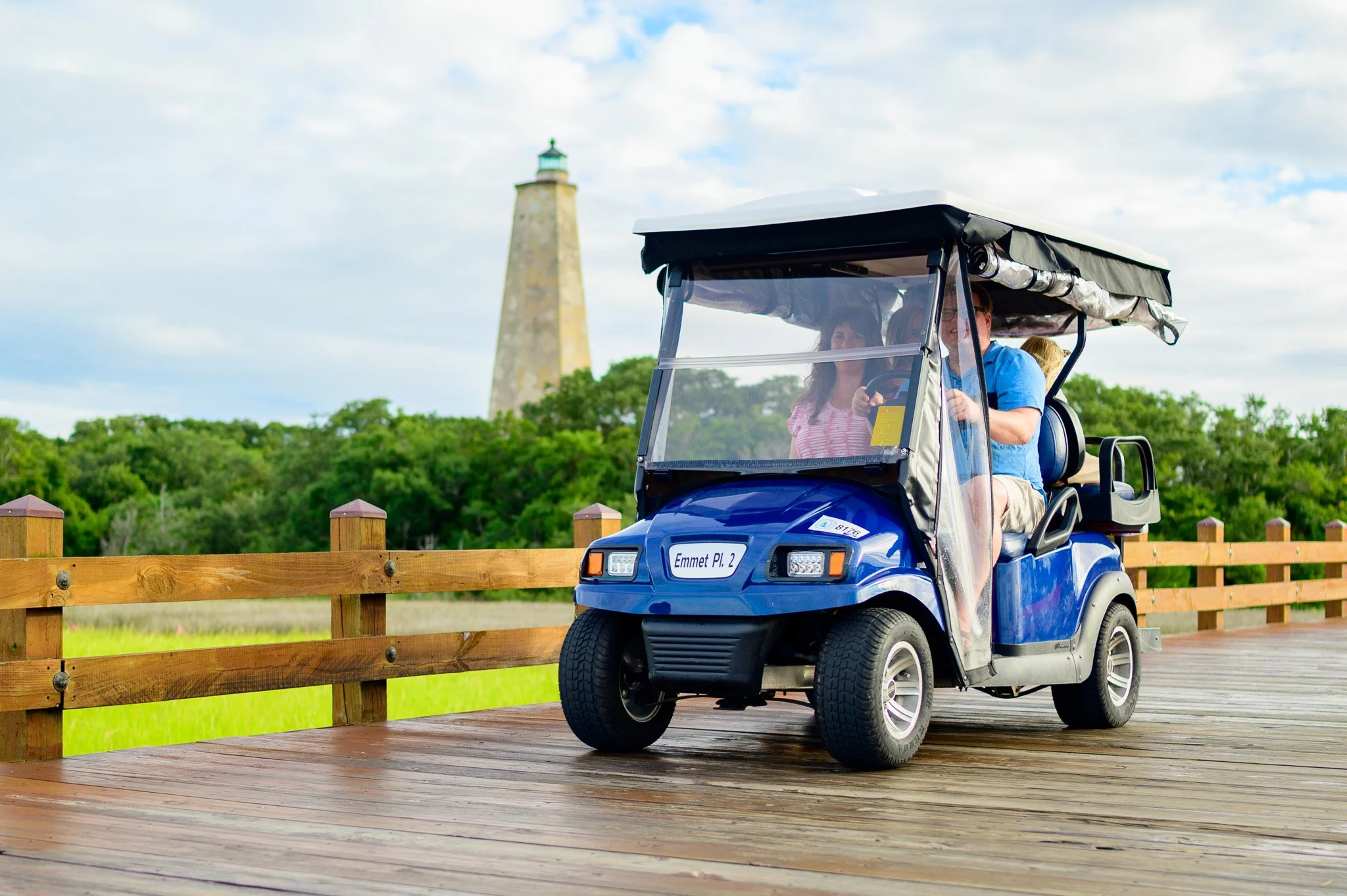 Visitors exploring Bald Head Island by golf cart with Old Baldy Lighthouse in the background.
