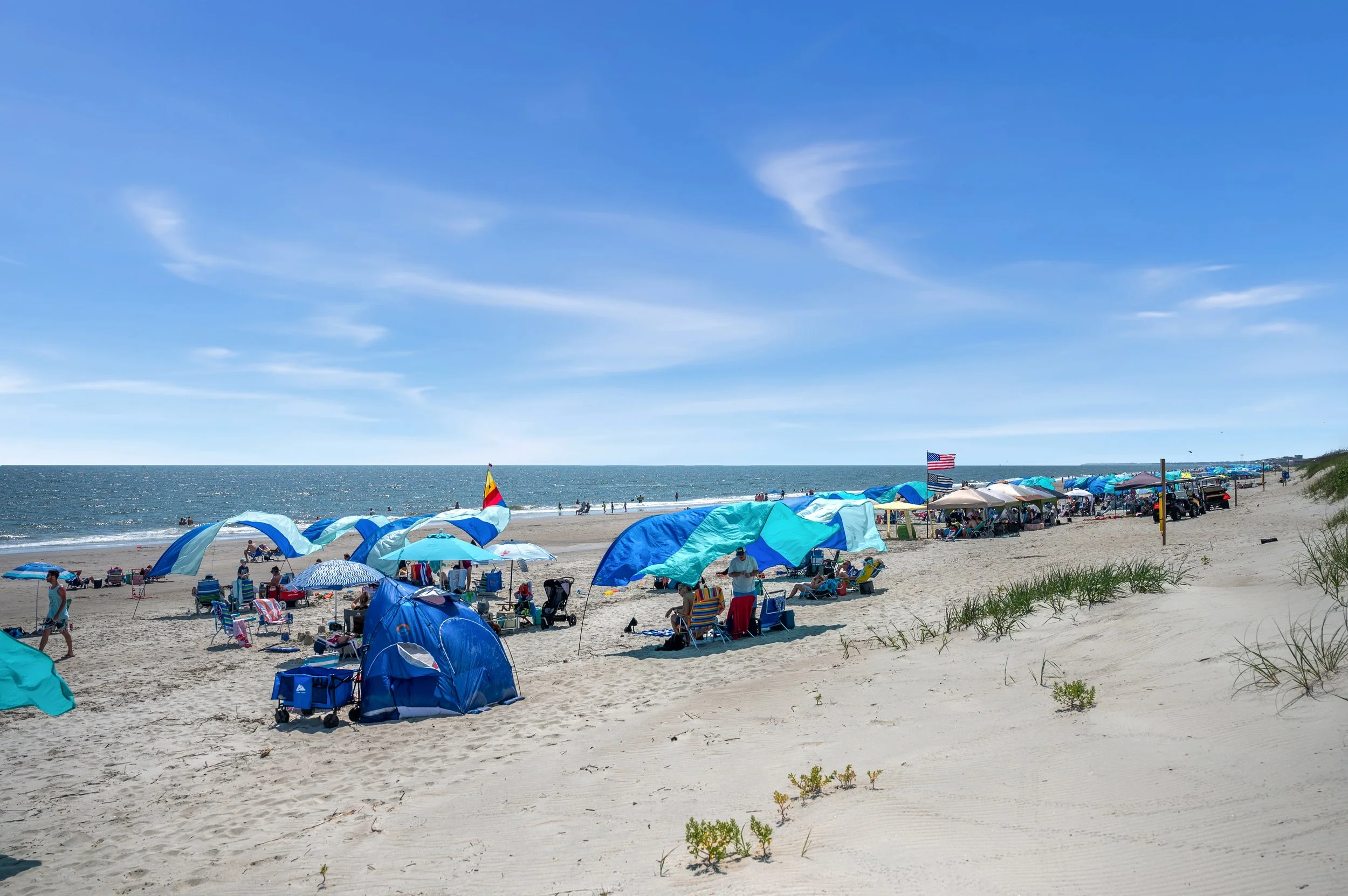 Families enjoying a sunny beach day on Oak Island, North Carolina, with umbrellas and chairs along the shoreline.