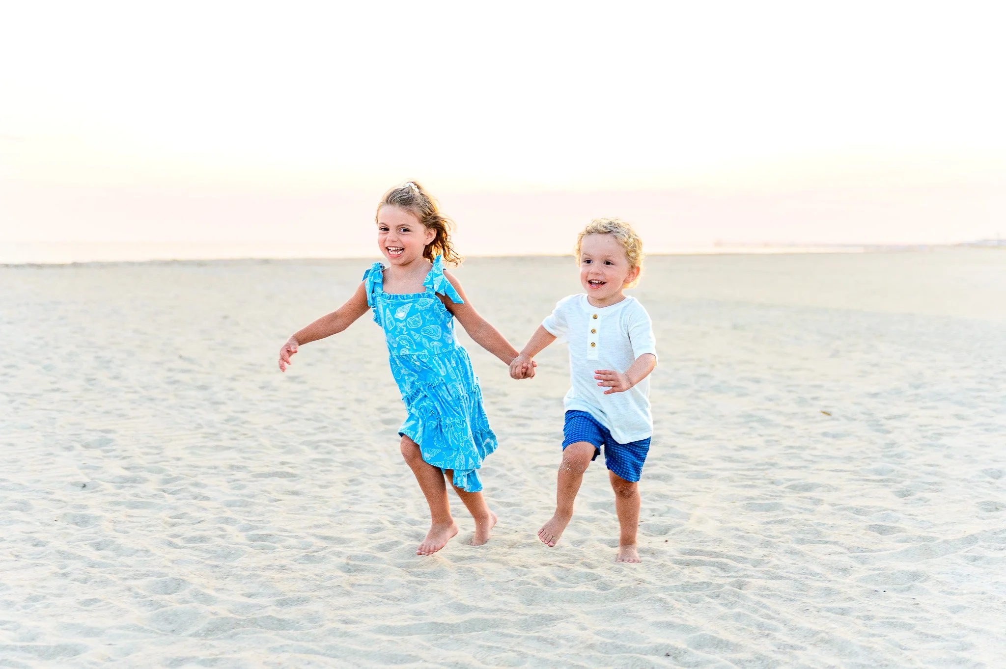 A brother and sister run along the beach during a family photo session in Caswell Beach on Oak Island