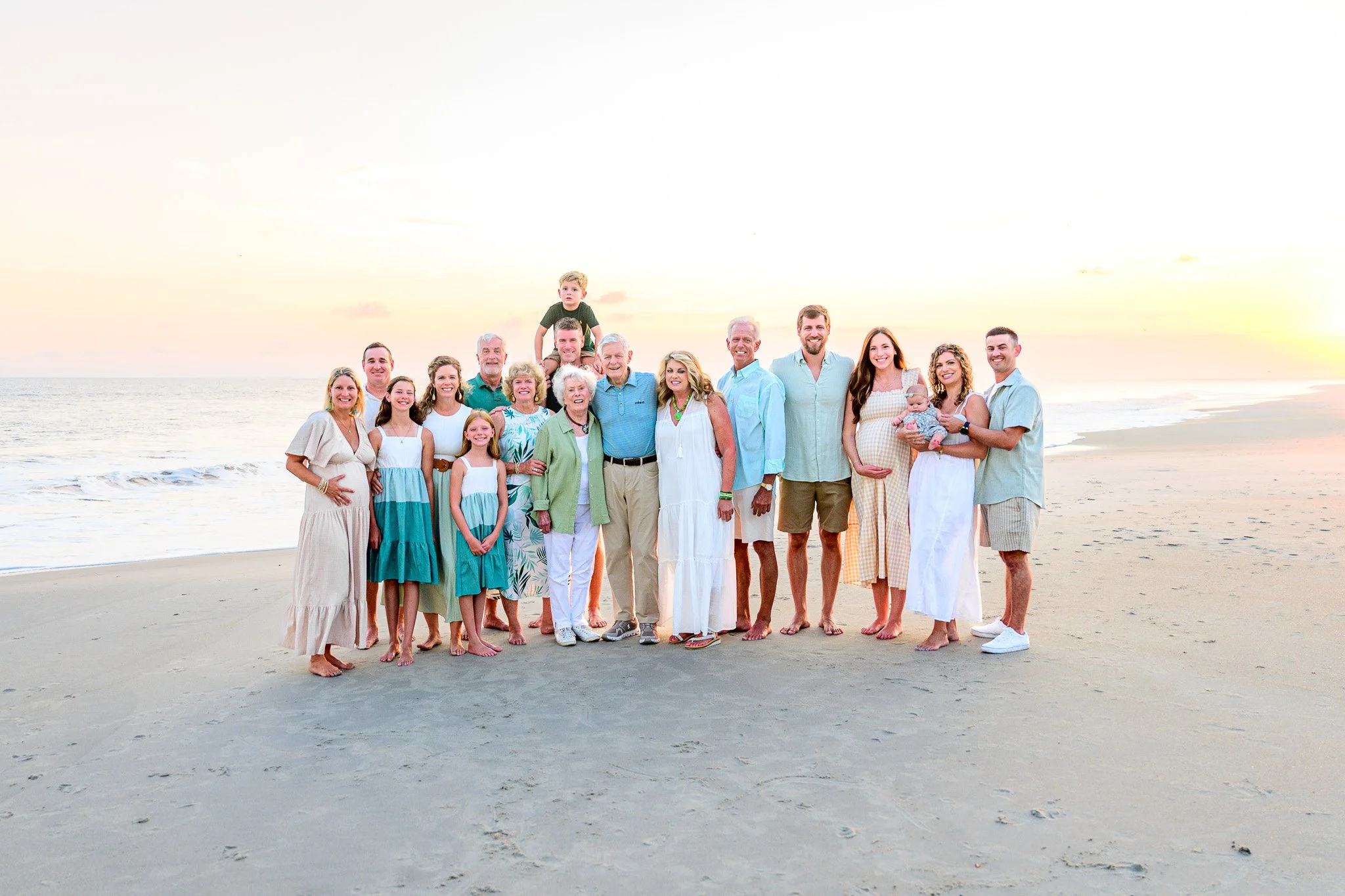 Multi-generational family posing for sunset beach photos during a vacation on Oak Island, North Carolina.