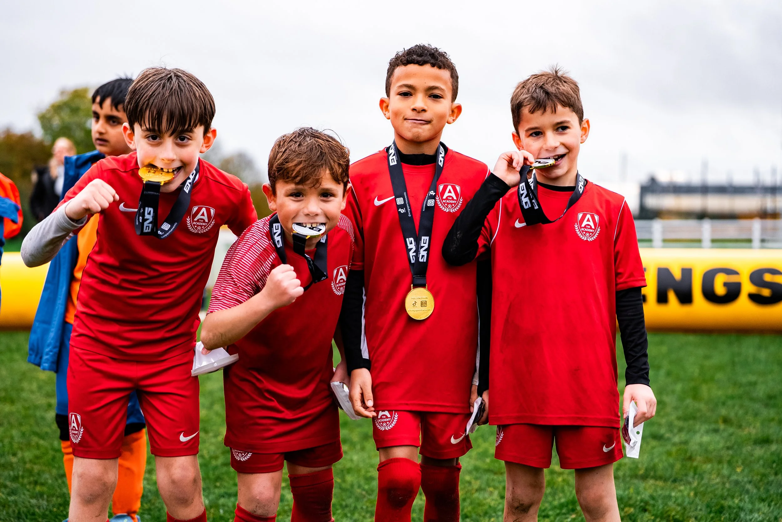 Group of young boys in red soccer uniforms with medals around their necks, celebrating on a soccer field.