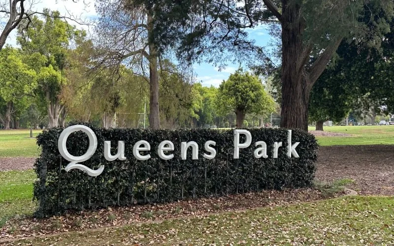 A photo of a hedge in Queens Park Toowoomba with the sign reading 'Queens Park'.