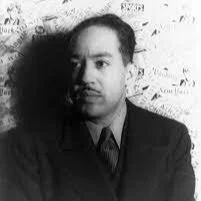 Black and white photo of a man in a suit with a serious expression, standing against a textured background.