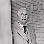 Black and white photo of a man in a suit standing near a brick wall.