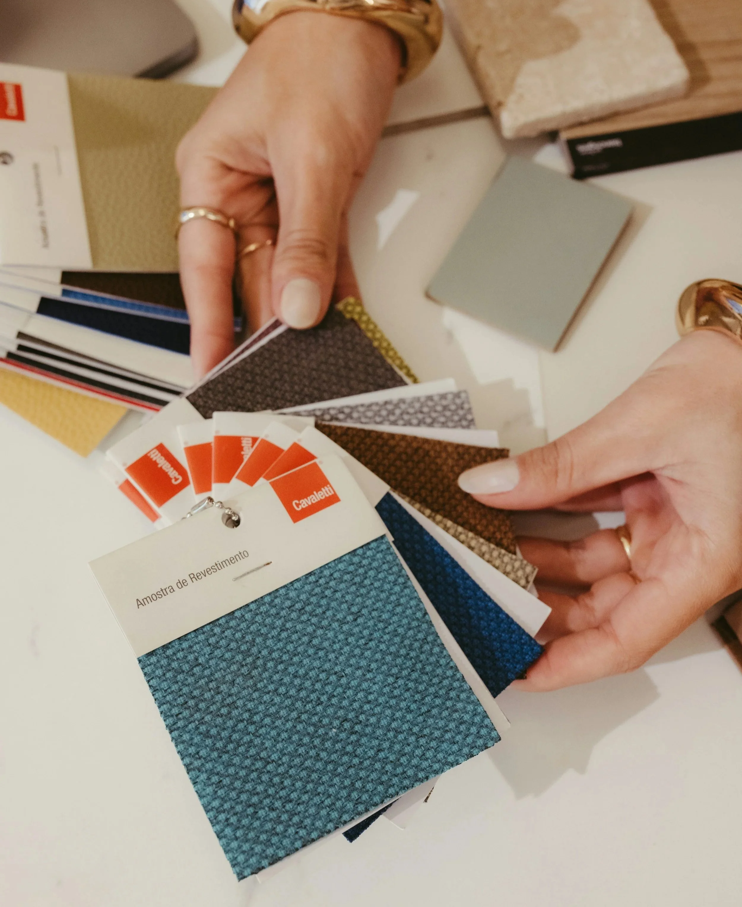 Close-up of a person's hand holding color sample cards of various fabric textures and colors, with a sample of gray textured fabric in the foreground.