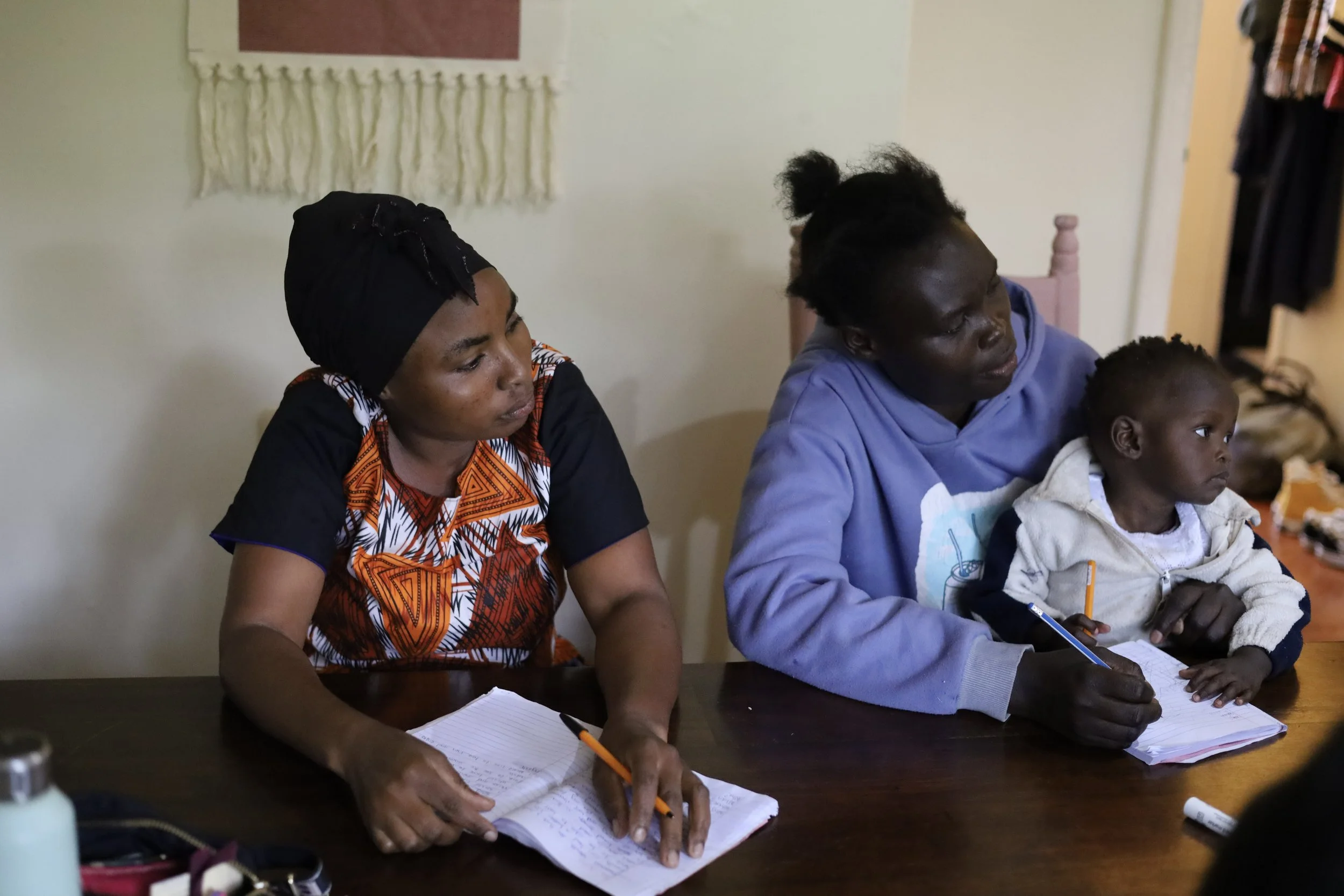 Two women and a young girl sitting at a table, taking notes and engaged in an activity.