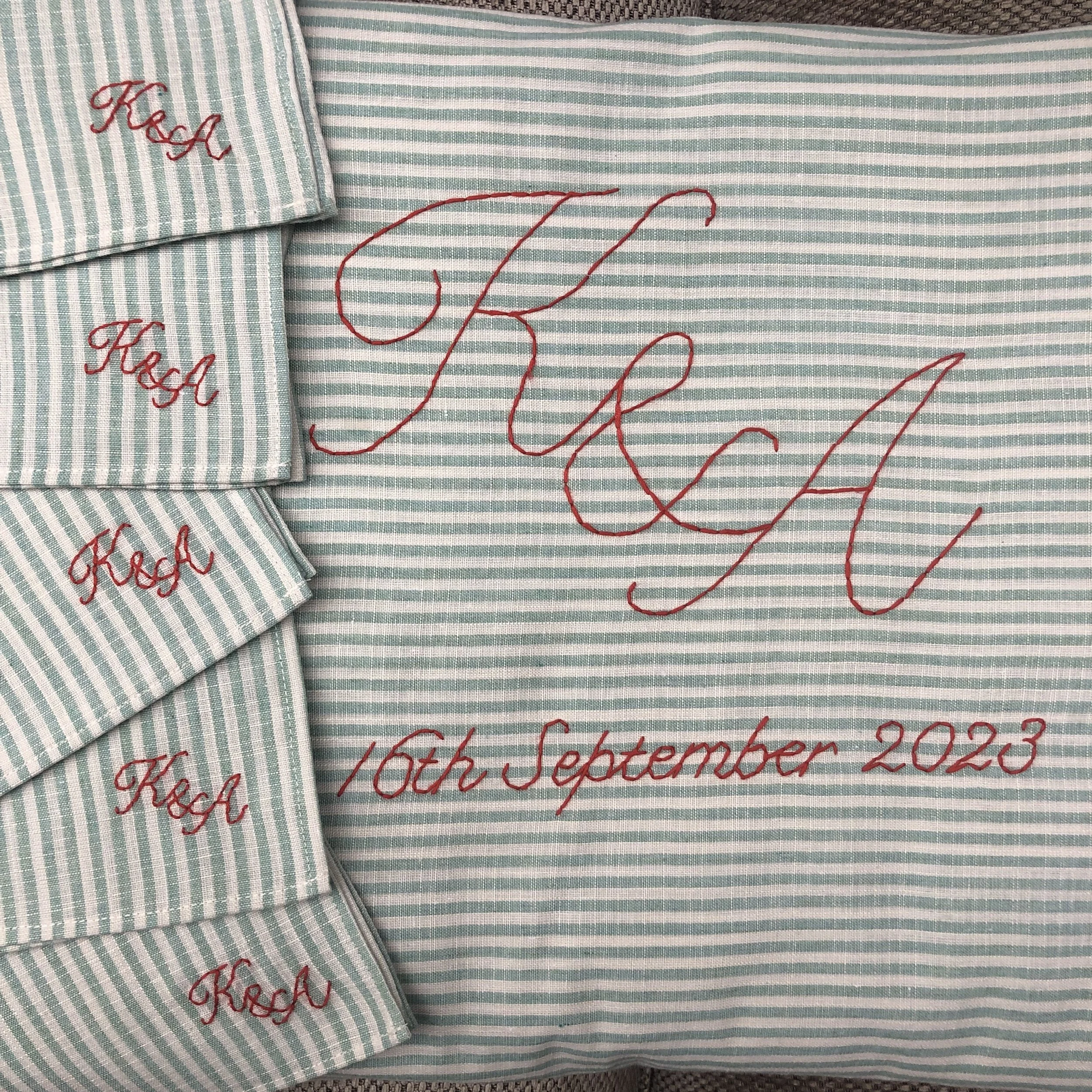A light blue and white striped fabric with red embroidered text. The fabric features a large, stylized word 'HUG' and the date '16th September 2023'. On the left side, there are several smaller fabric swatches with red embroidery spelling 'KraK'.