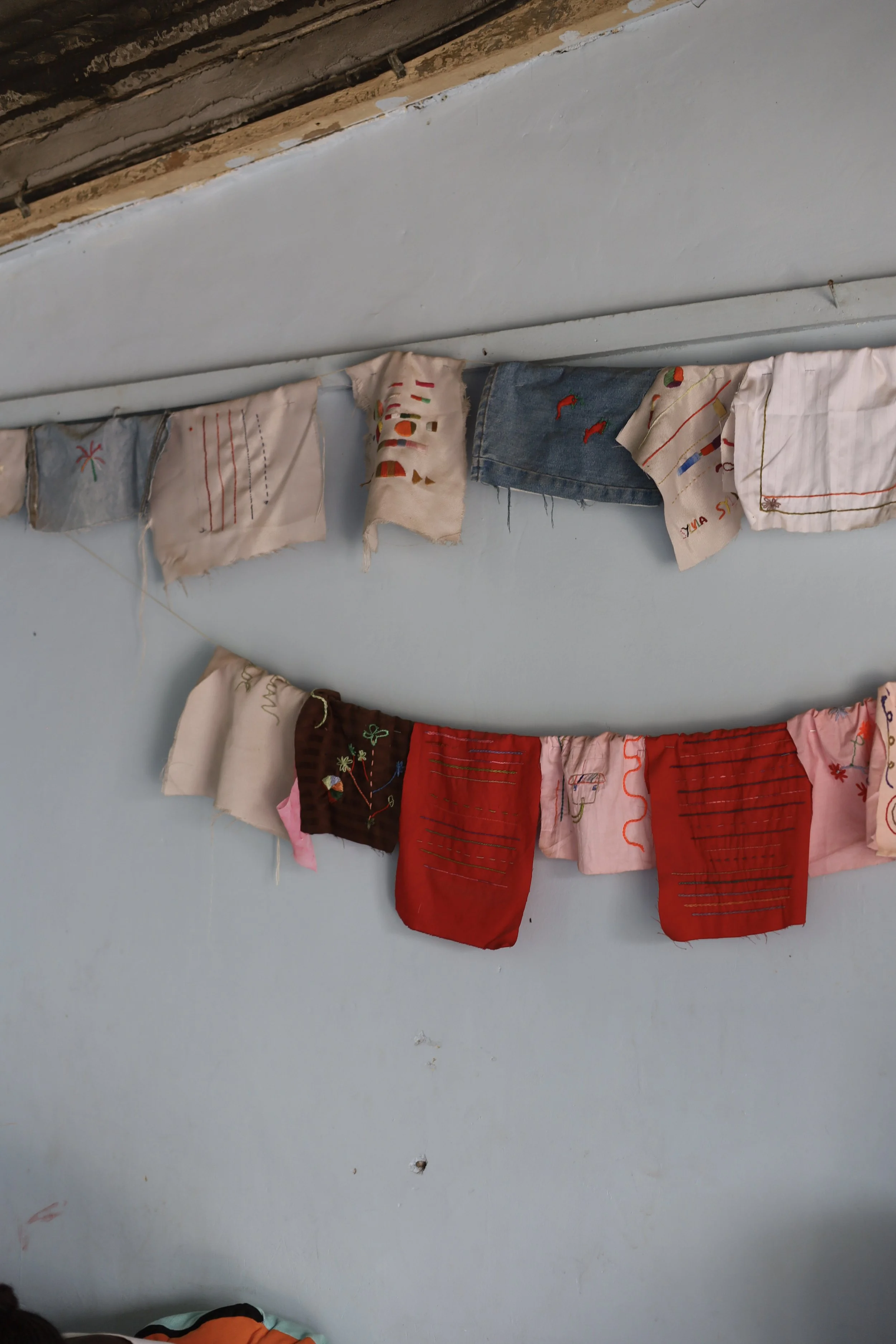 Colored fabric scraps with embroidered and stitched designs hanging on a wall.