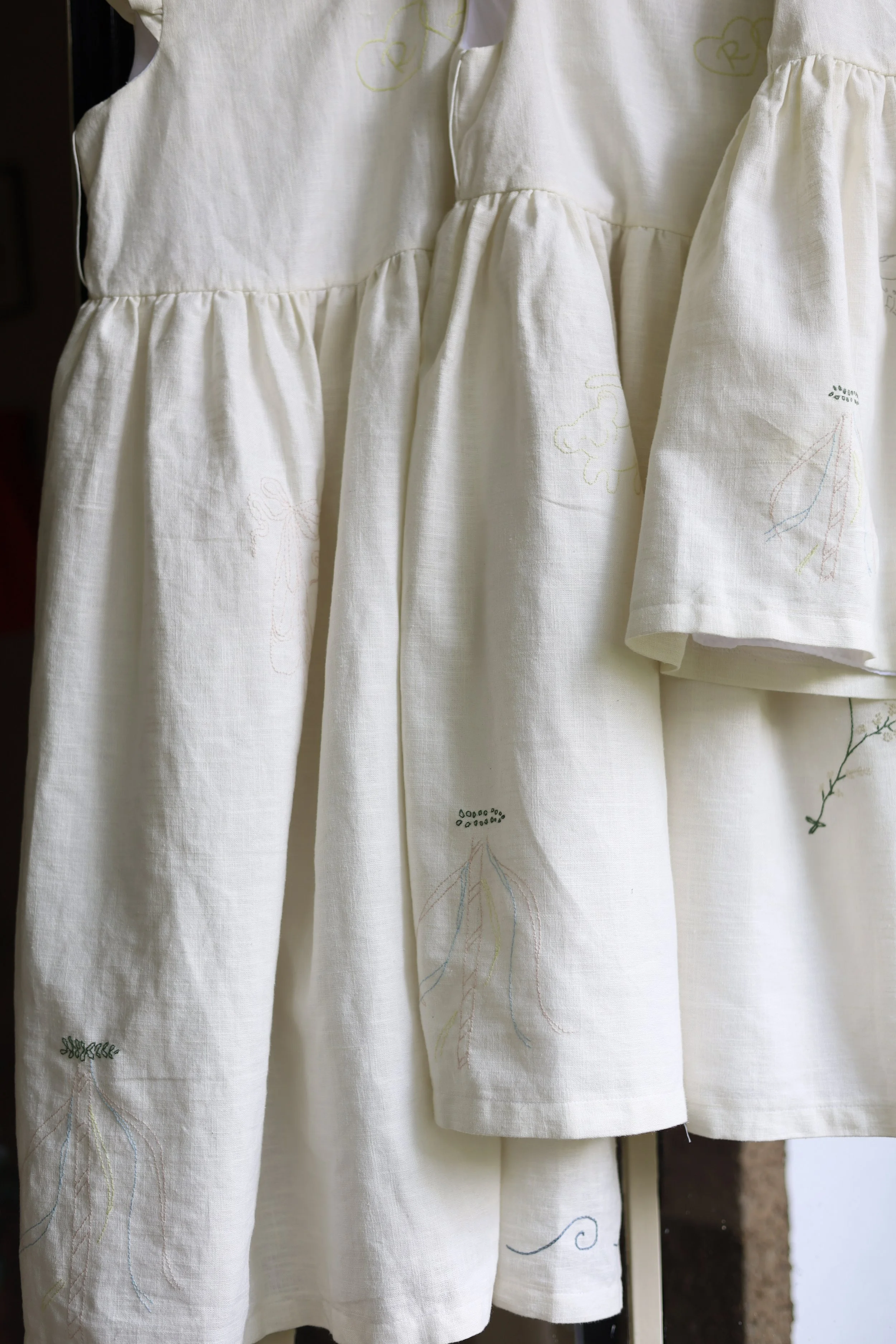 Close-up of a white linen dress or curtain with embroidered patterns of animals, leaves, and abstract designs.
