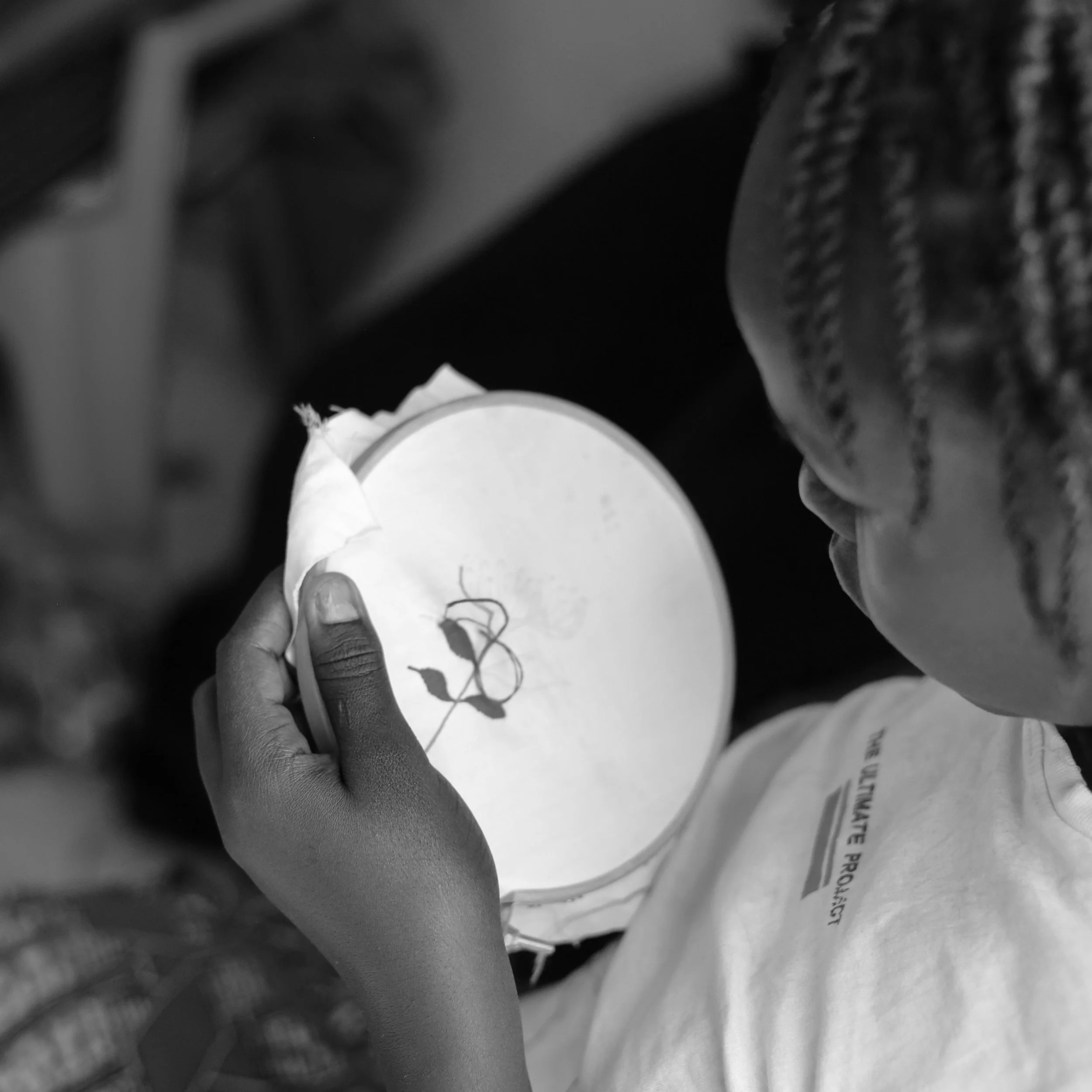 A person with braided hair holding an embroidery hoop with a design of a flower.