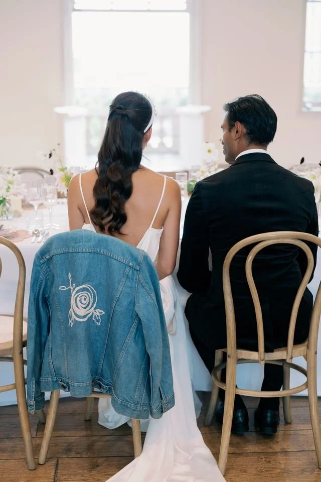 A woman and man sitting at a decorated table, facing away from the camera, with a denim jacket hanging on a chair in front of them.
