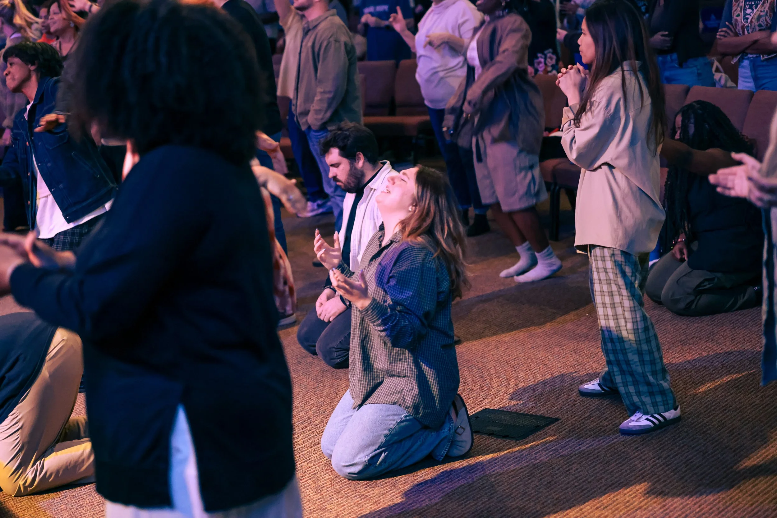 People praying and worshipping during a religious service, with some kneeling and others standing with their hands raised.