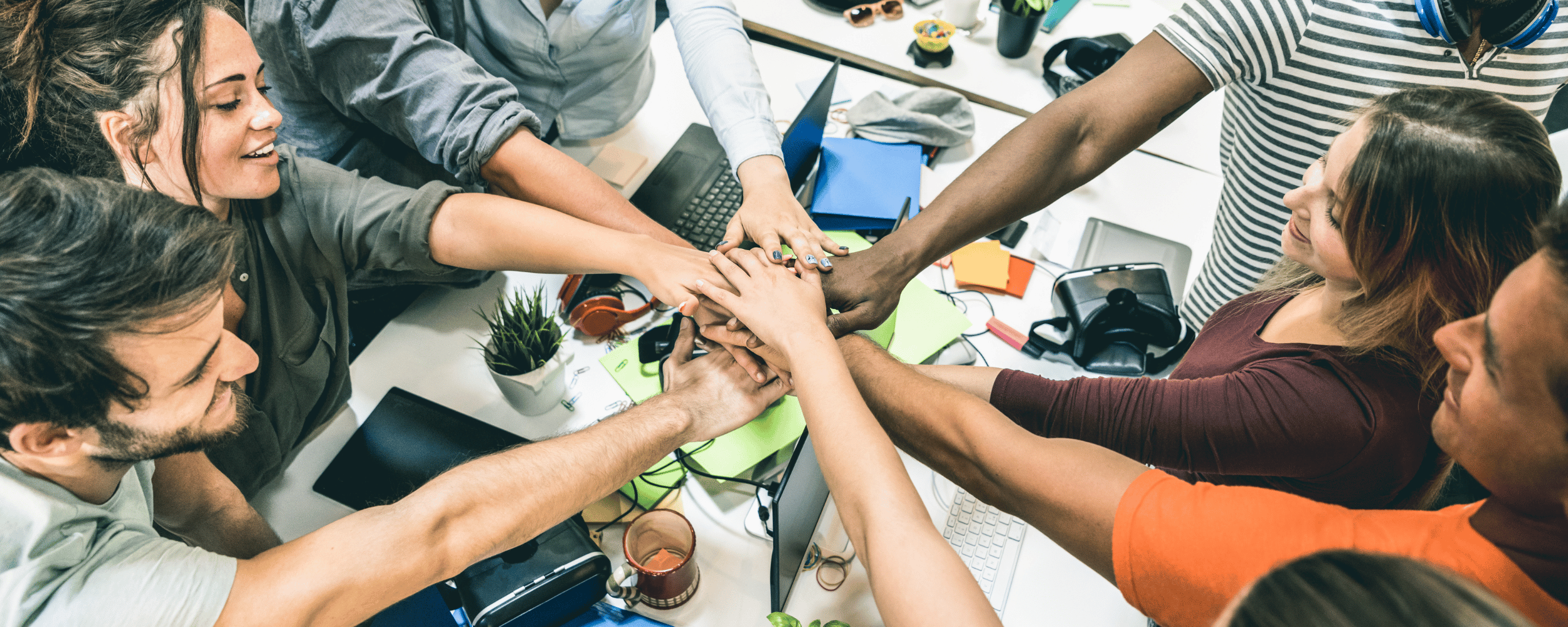 Group of diverse people putting their hands together in a show of teamwork in an office setting.