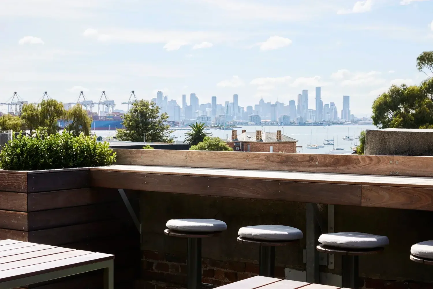 Outdoor seating area overlooking the water with a city skyline and boats in the distance.
