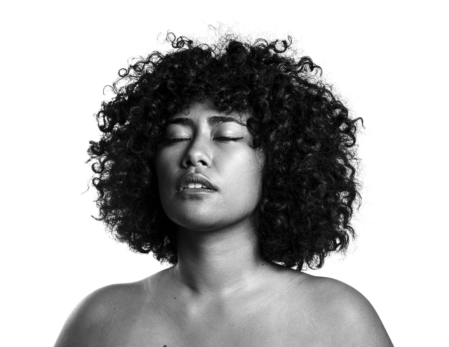 Black and white portrait of a woman with curly hair and closed eyes.