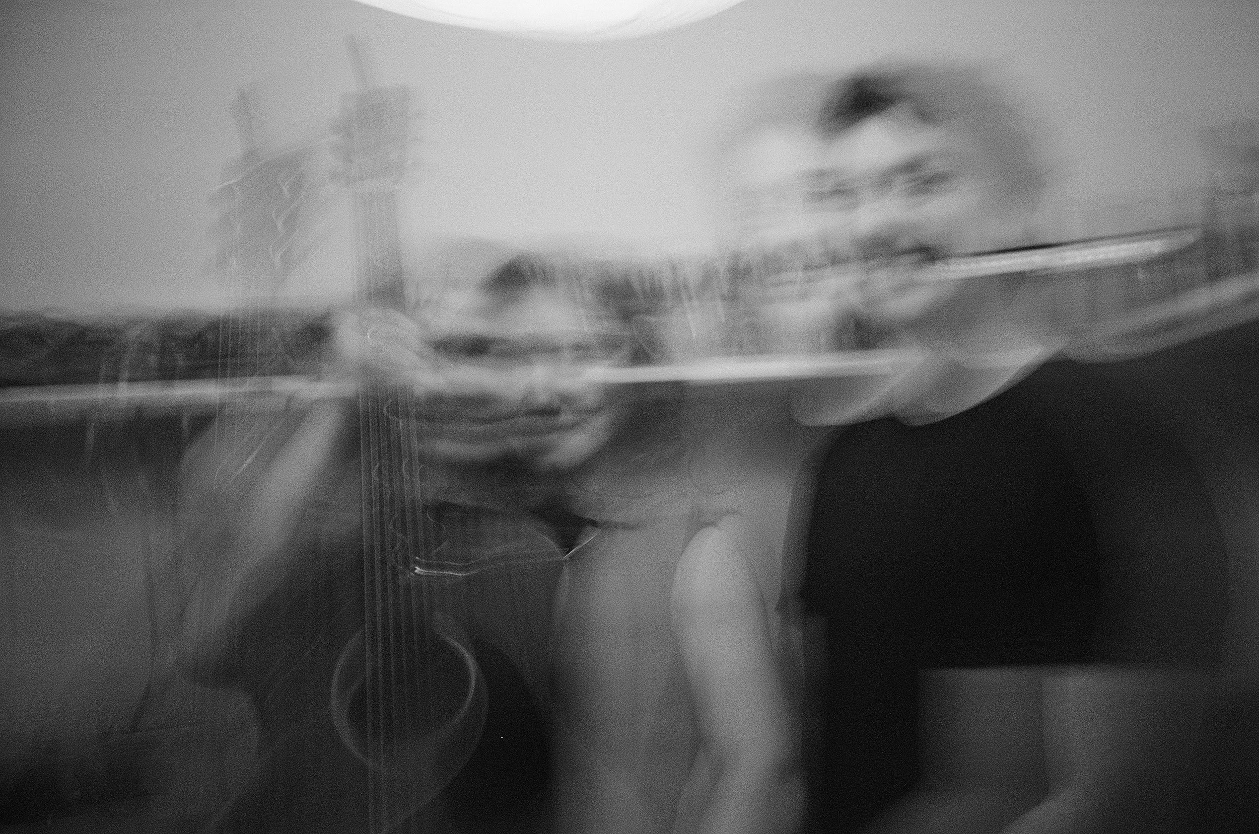 A blurry black-and-white photograph showing a person's face and hands. The person appears to be touching their face, with the image capturing motion or blur, making details indistinct.