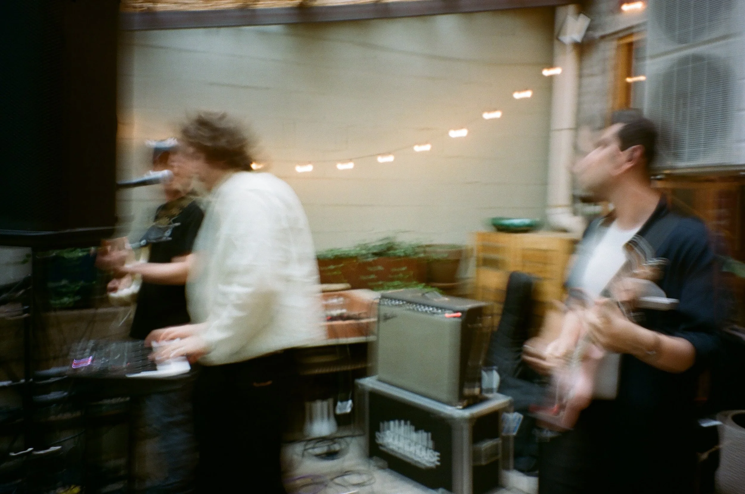 People at a party or gathering, standing near a counter with drinks, in an indoor setting with string lights hanging on the wall.