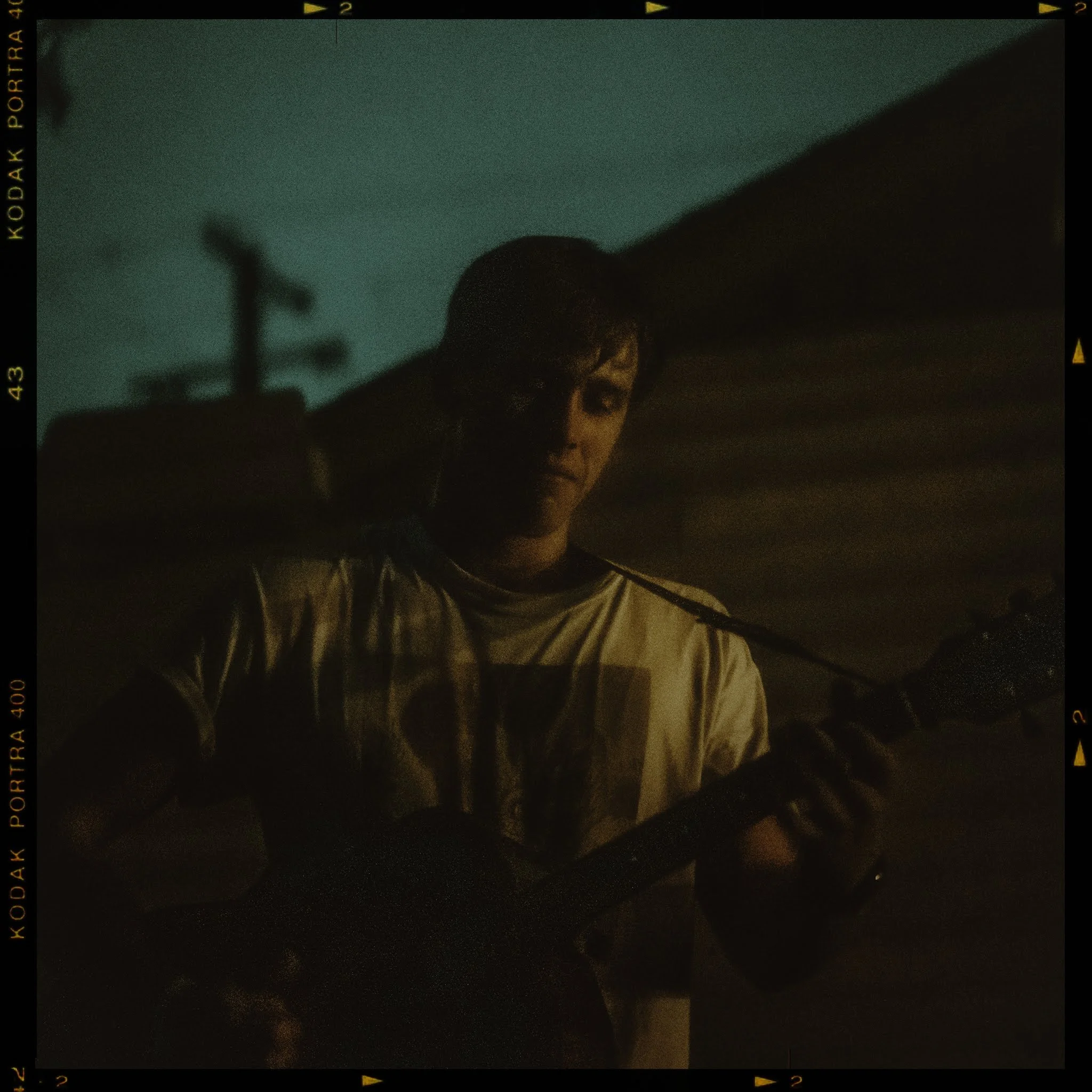 A person wearing glasses and a beige jacket looks downward, with a teal-colored sky in the background at night.