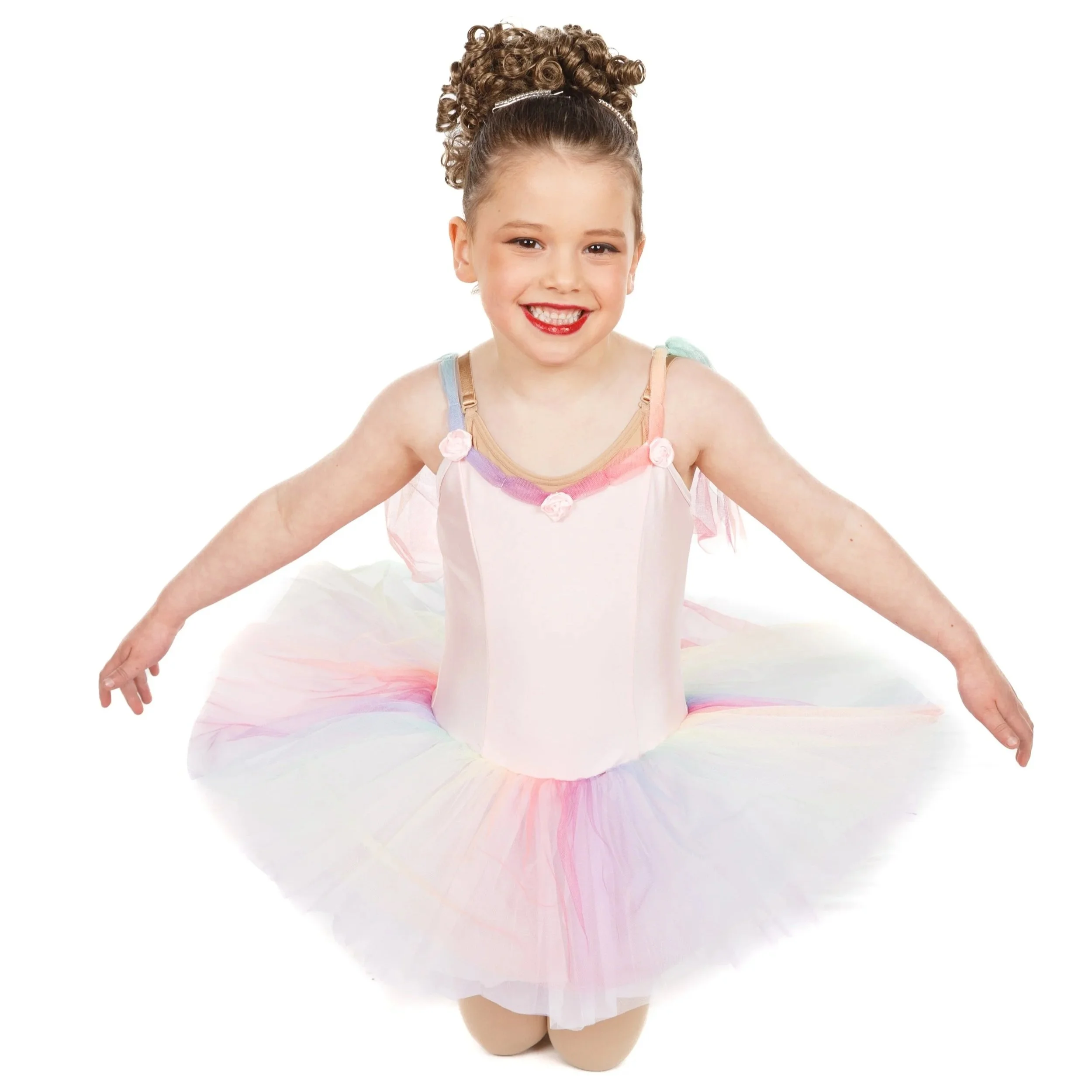 Dancer smiling in a pastel-colored ballet tutu, kneeling with arms extended, against white background.