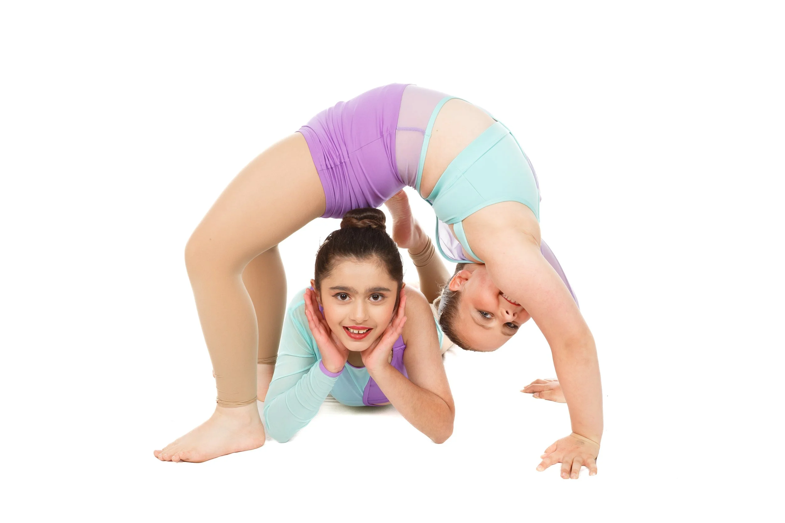 Two dancers in pastel-colored athletic outfits are performing an acrobatics pose together on a white background, with one girl supporting the other in an bridge position.