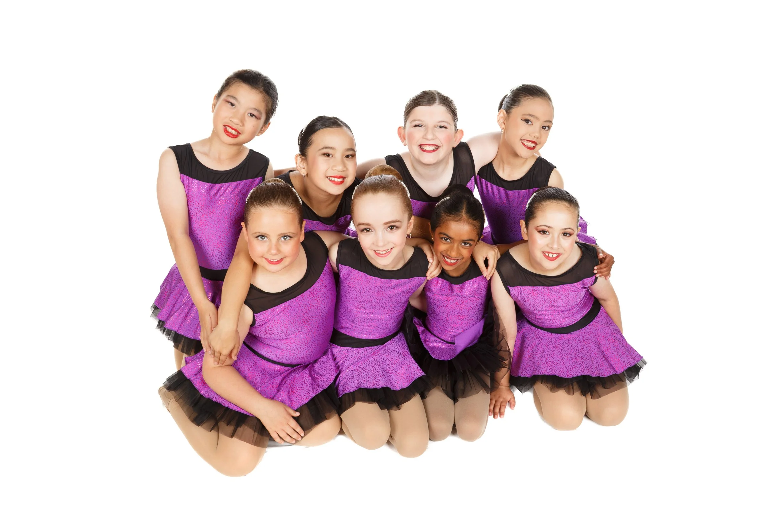 Group of dancers in matching purple and black dance costumes, smiling and posing together.