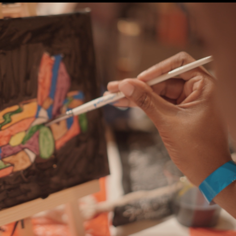 Close-up of a person's hand painting on a small canvas with a paintbrush