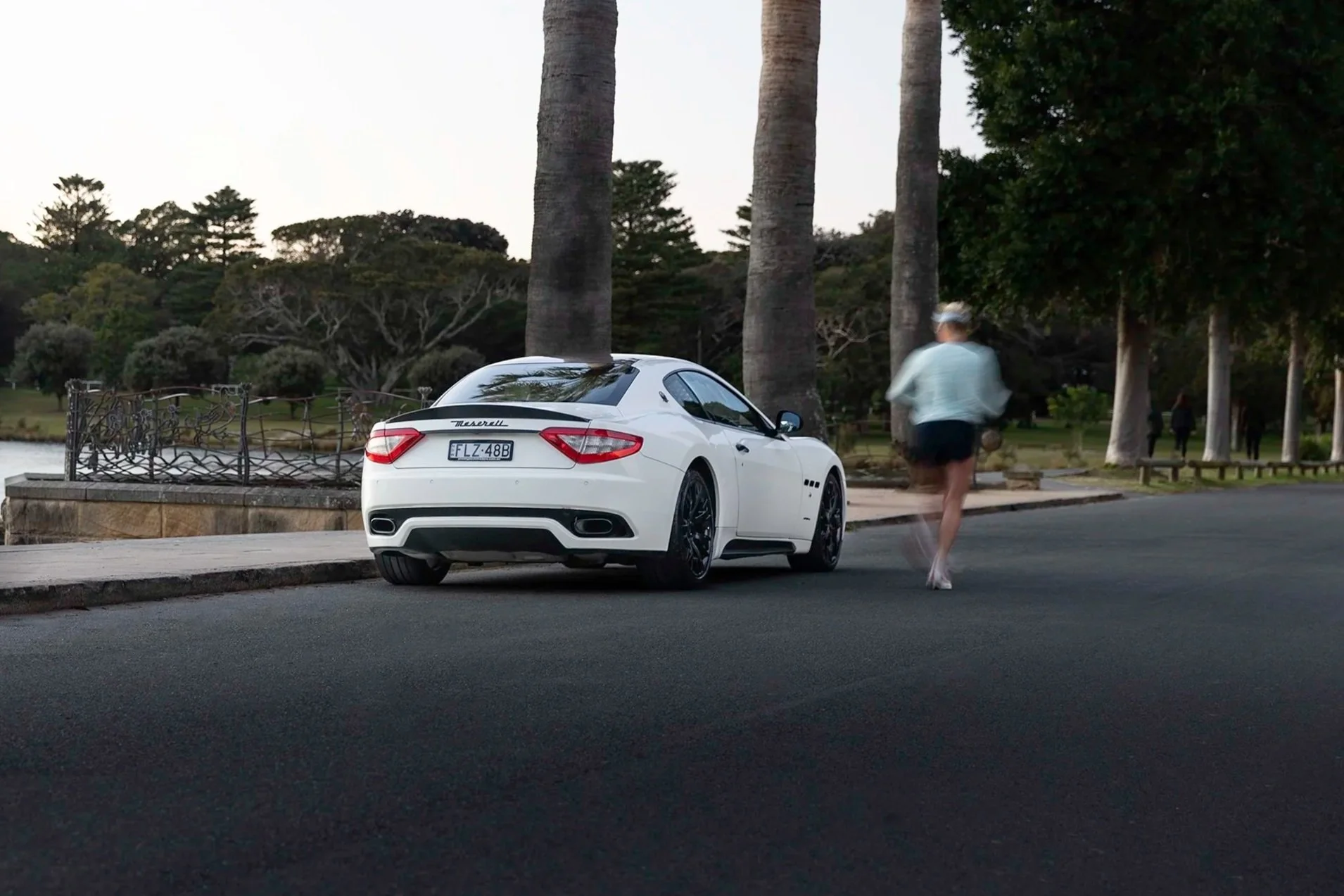 Automotive photography of a white Maserati GranTurismo S driving away along a palm-lined path, Sydney