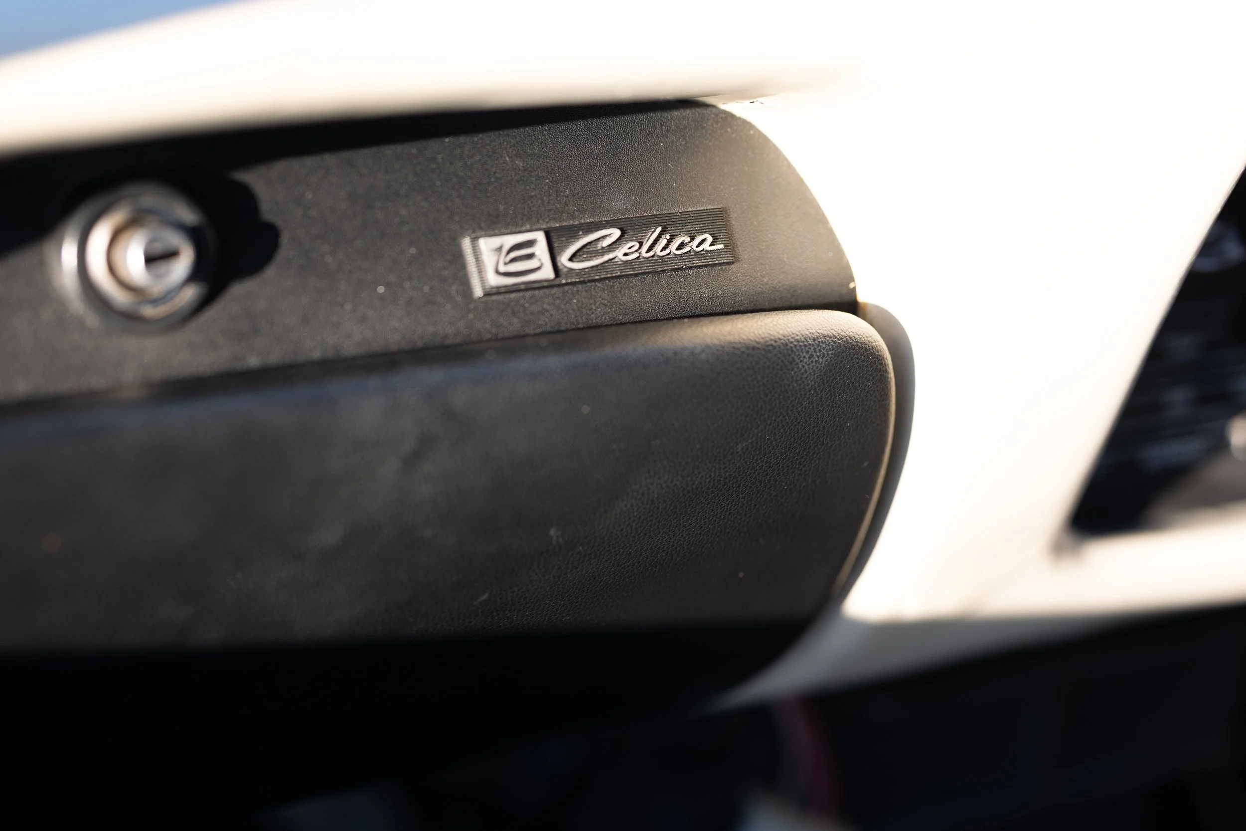 Toyota Celica script emblem on the glovebox of a TA22 1600GT interior. Classic Japanese car interior detail photography.