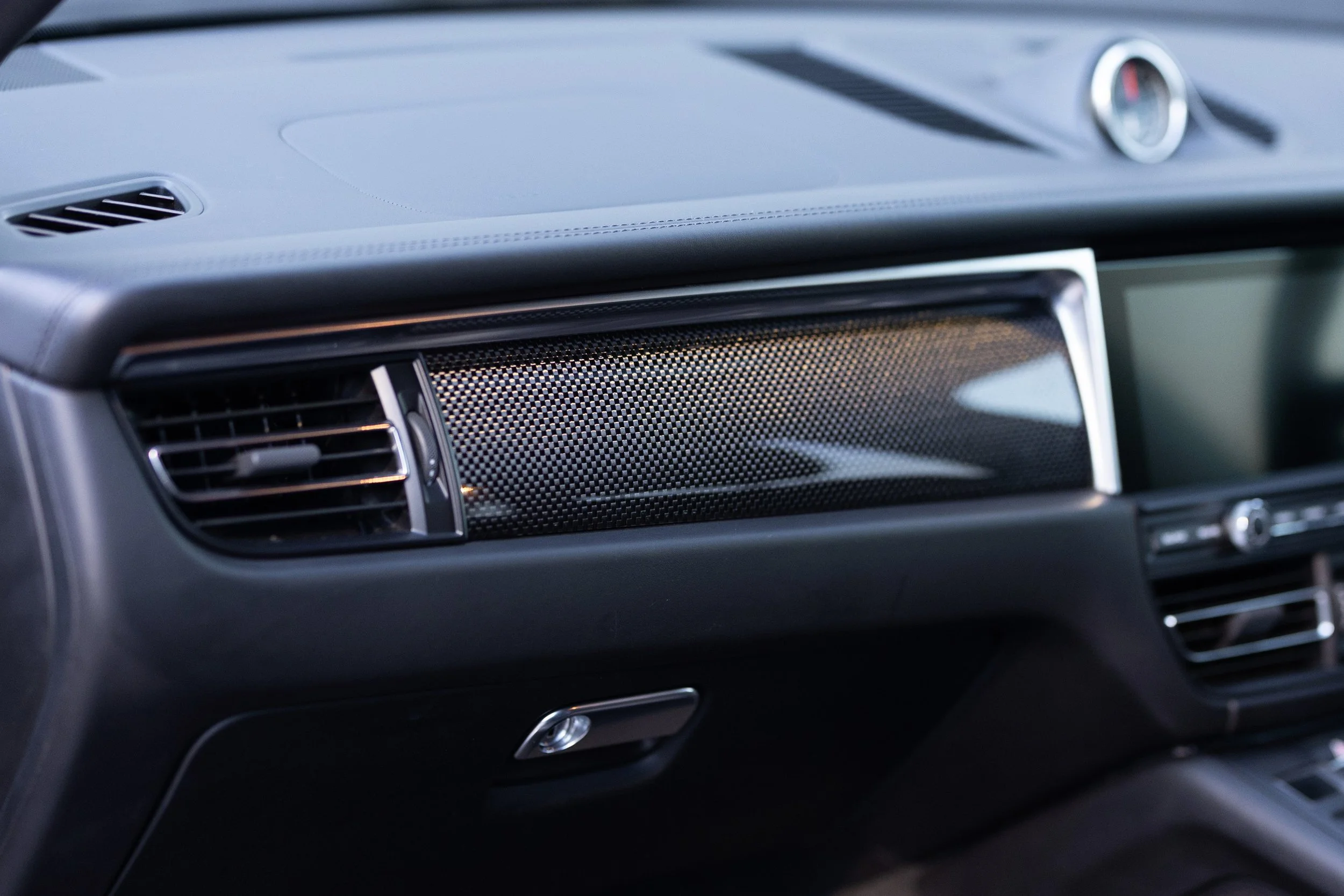 2019 Porsche Macan S passenger side dashboard carbon fibre trim panel and speaker vent detail with Sport Chrono clock visible
