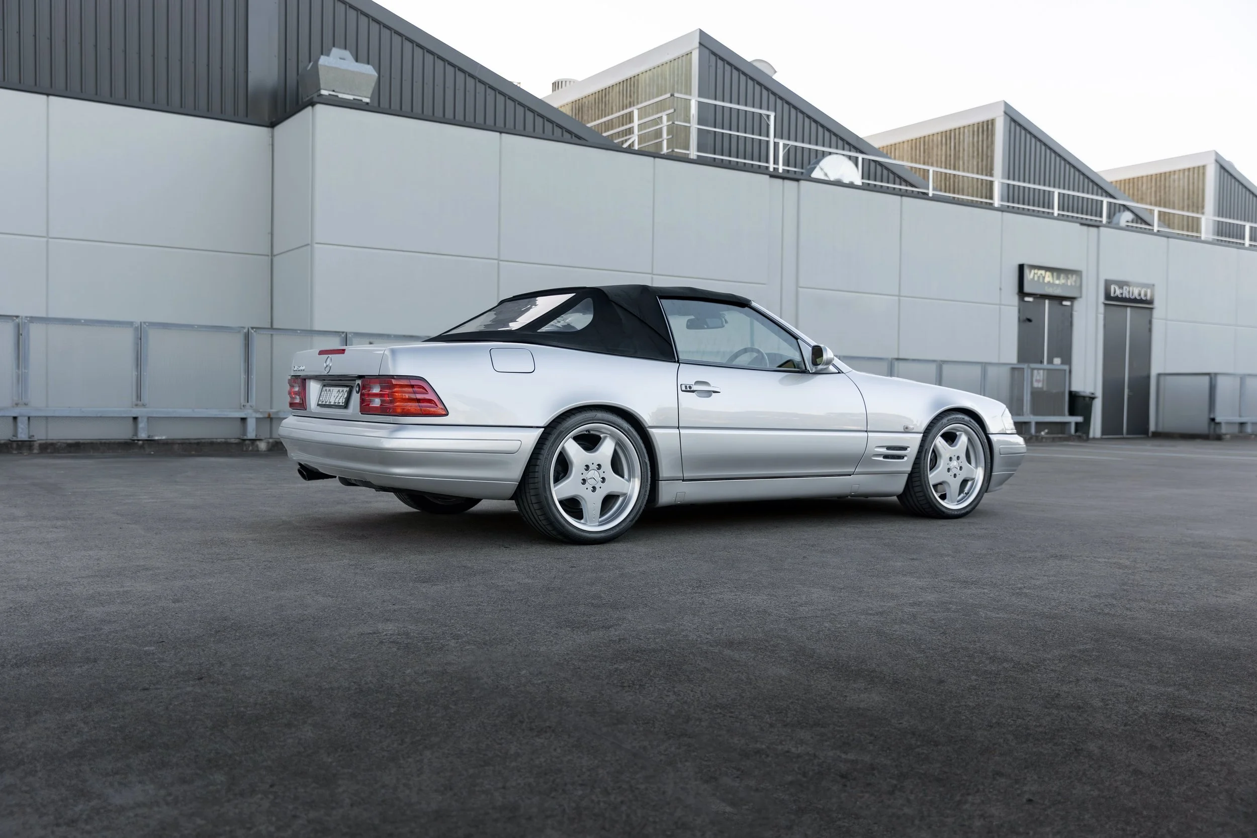 Silver 1999 Mercedes-Benz SL 500 R129 rear three-quarter against an industrial building, Sydney.