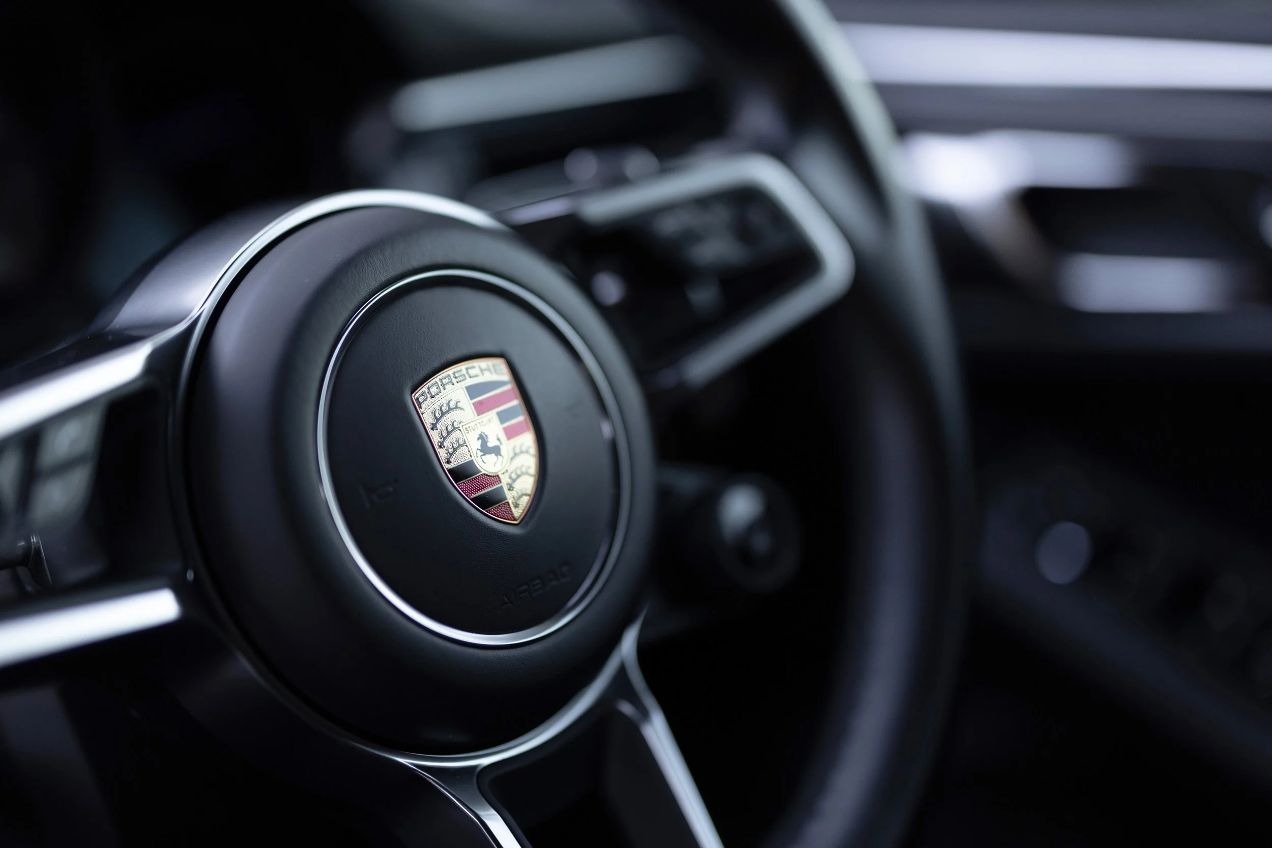 Porsche crest badge on multifunction sport steering wheel of 2019 Macan S, controls and dash in background
