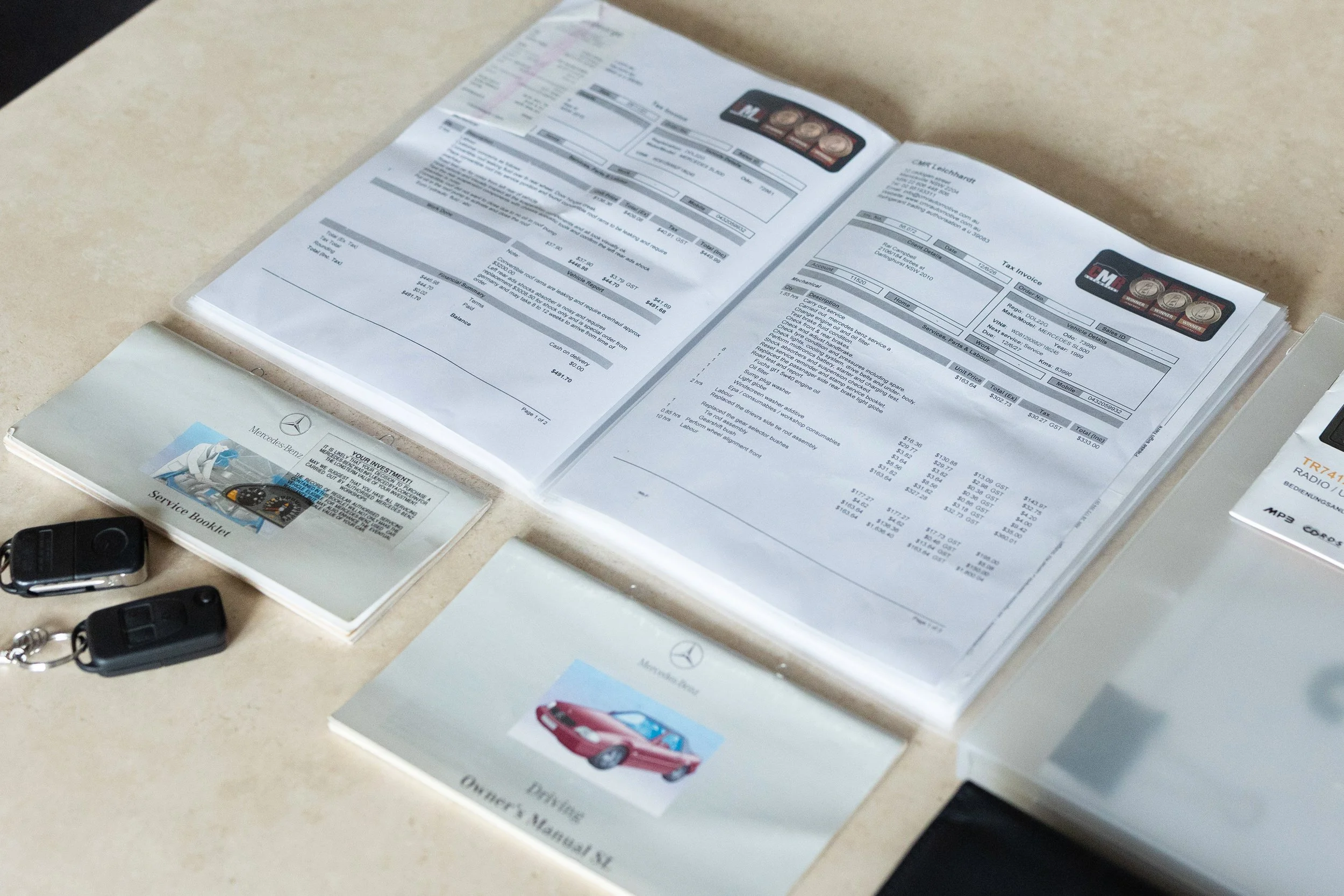 Open car service receipts, a Mercedes-Benz service booklet, and car key fobs on a light-colored surface.