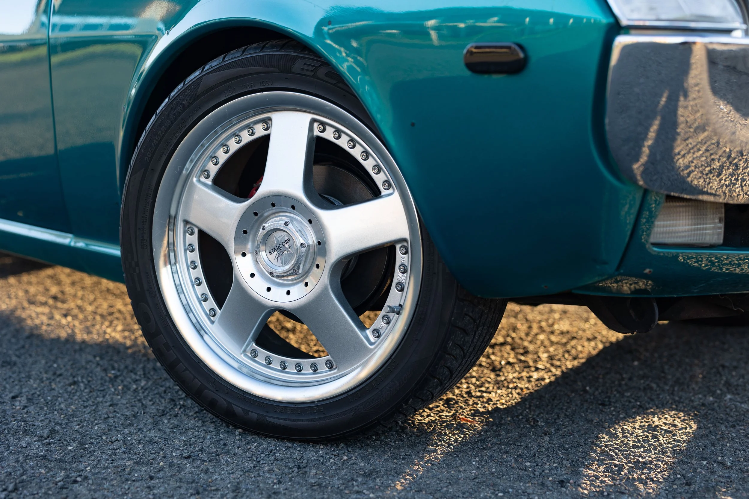 Starcorp deep-dish alloy wheel and Kumho tyre on a teal Toyota Celica 1600GT TA22, rear-quarter wheel detail automotive wheel photography.