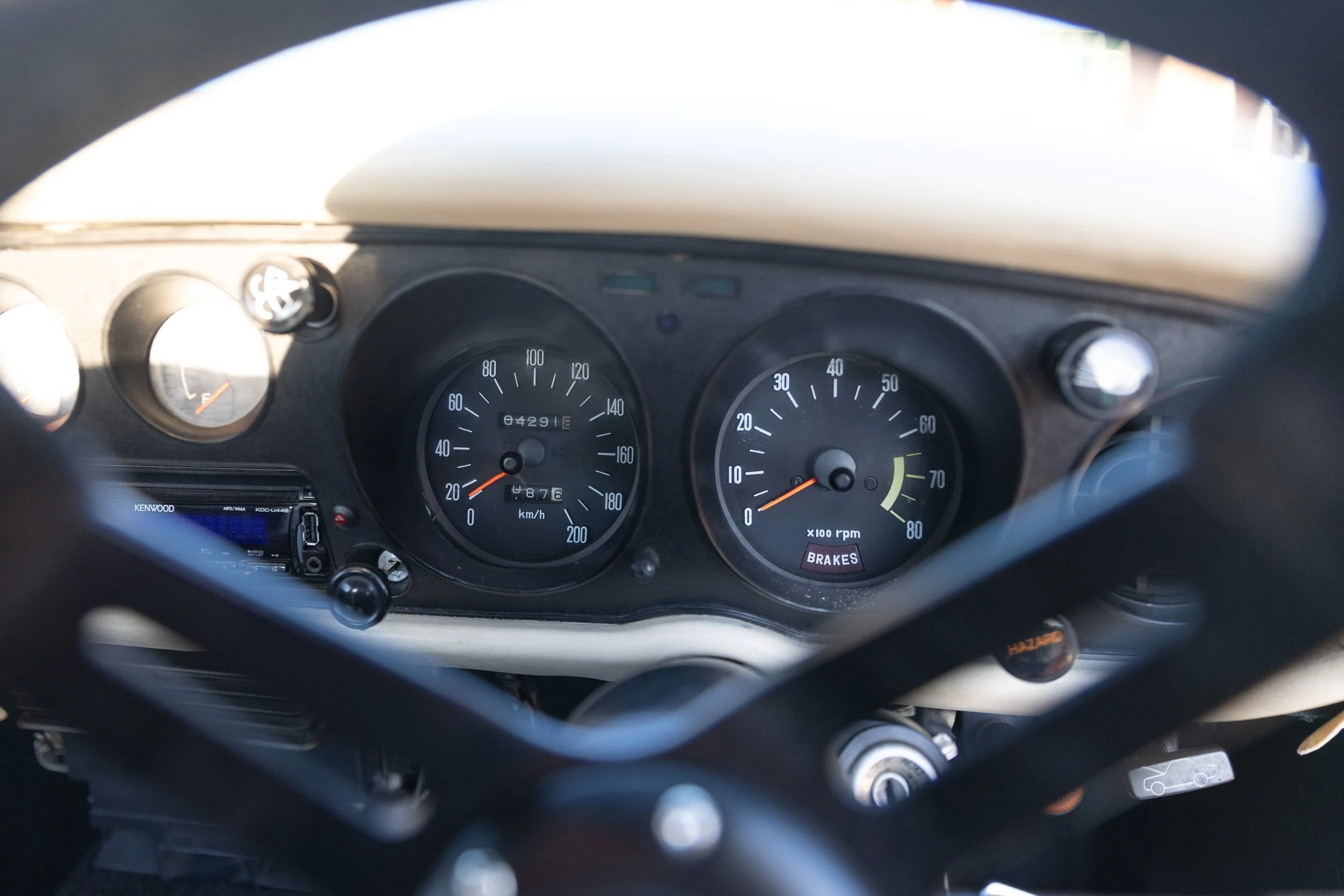 Toyota Celica 1600GT TA22 instrument cluster with 200 km/h speedometer and 8000 rpm tachometer through the steering wheel. Classic car interior photography.