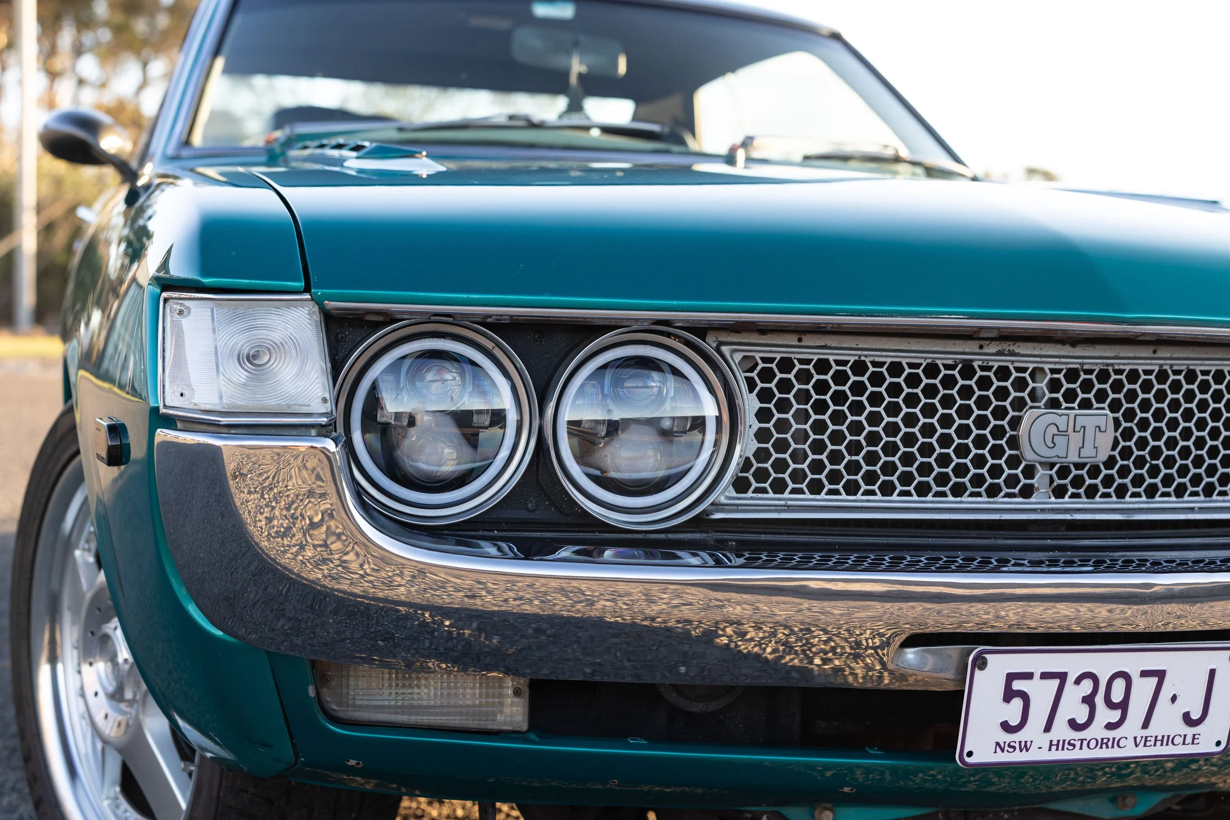 Close-up of a Toyota Celica GT grille and quad LED-projector headlight conversion with chrome bezels and honeycomb mesh classic car front-end detail photography.
