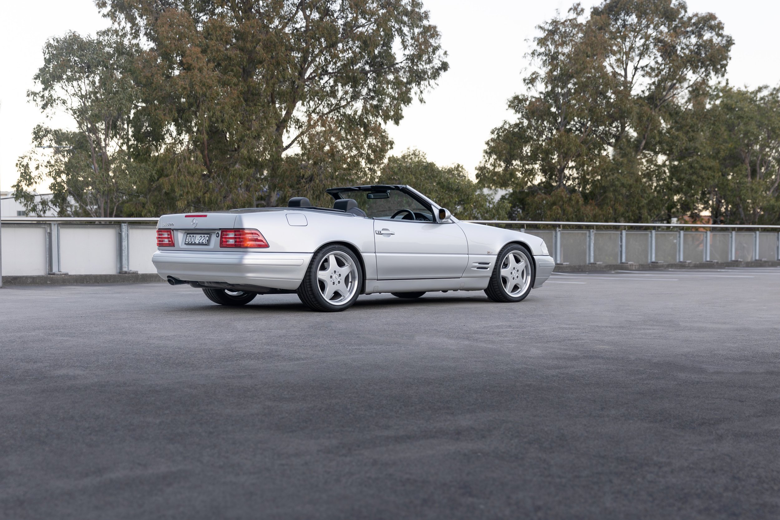 Silver Mercedes-Benz SL 500 (R129) rear three-quarter, wide rooftop view with trees, Sydney.