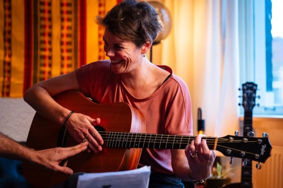 Cours de guitare à Saint-Gilles, Bruxelles: une élève souriante joue de la guitare acoustique pendant le cours