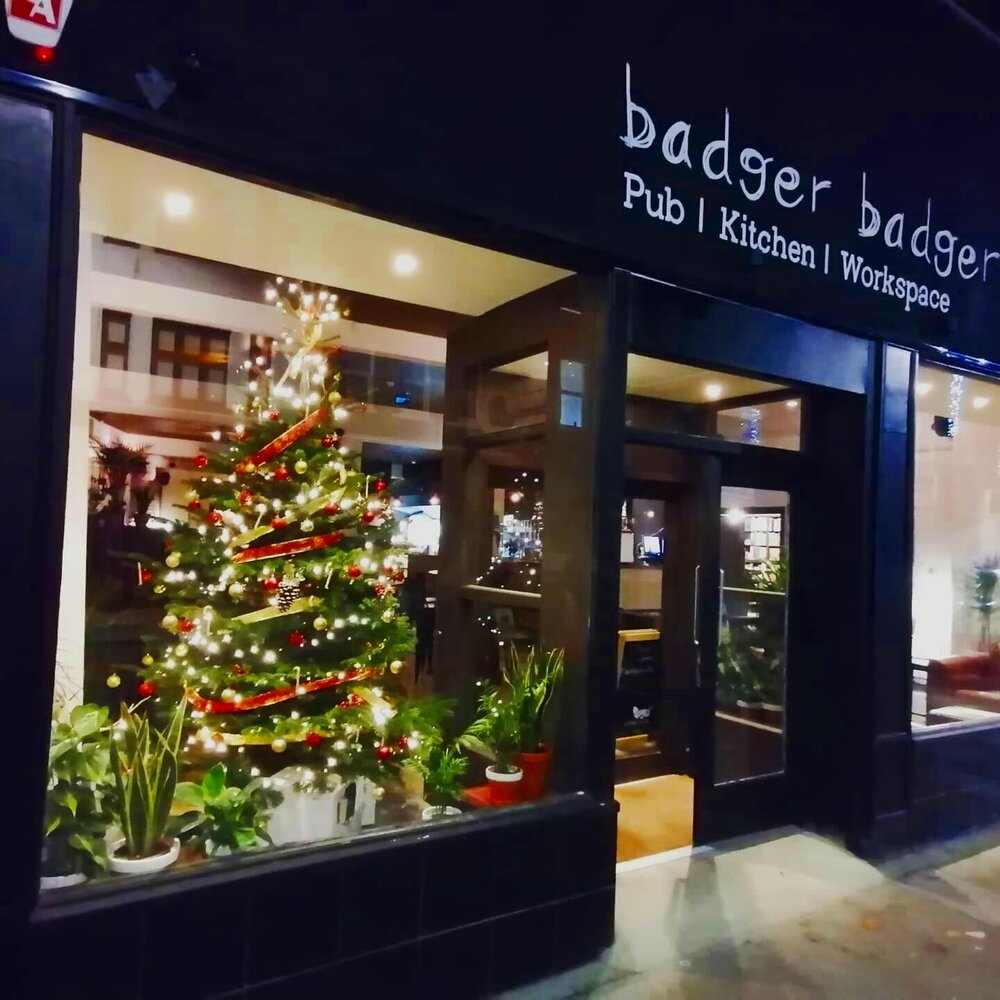 the outside of the Badger Badger pub building at night with a Christmas tree in the window -on Tally Workspace