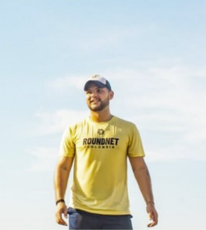 A man in a yellow t-shirt with the words "Roundnet Georgia" on it, standing outdoors against a blue sky.